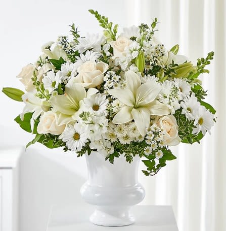White floral arrangement in a white vase with roses, lilies, and daisies