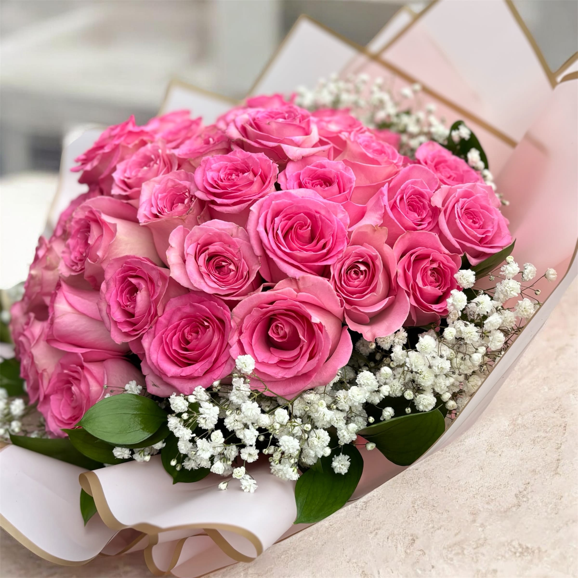 Blushing Elegance – 25 Pink Roses - Soft, romantic, and timeless. Our Blushing Elegance bouquet features 25 premium pink roses beautifully hand-wrapped and finished with a delicate rim of fresh baby’s breath. The lush circle of baby’s breath enhances the natural beauty of each bloom, creating a full, cloud-like frame around the roses.   Perfect for birthdays, anniversaries, congratulations, or simply to show someone how much they mean to you. This hand-tied bouquet is designed to impress from every angle and makes a stunning statement of love and appreciation.    25 premium pink roses   Accented with fresh baby’s breath   Elegant hand-wrapped presentation   Perfect for any special occasion