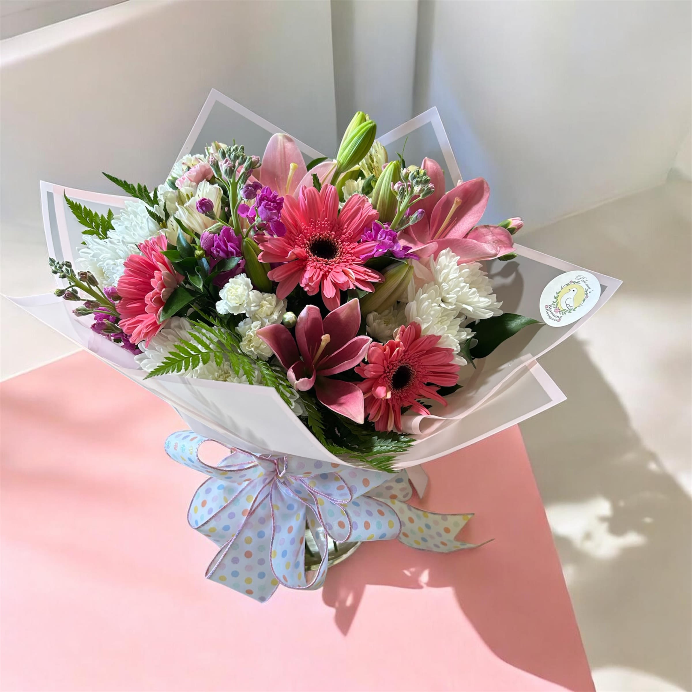 You The Best Bouquet  - Bright pink gerbera and lilies with white and purple accents in a clear vase, wrapped with pastel polka-dot ribbon-cheerful, layered bouquet perfect for birthdays or thank-you moments.