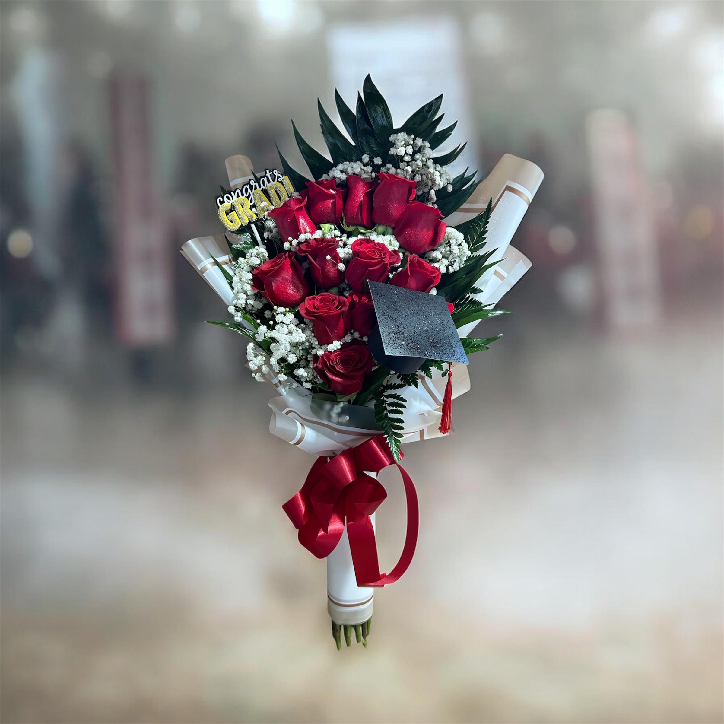  Blue &amp; Gold Celebration Bouquet - Deep red roses with white fillers and dark greenery, wrapped in white paper with a red satin ribbon and a black graduations cap topper-bold, romantic, and perfect for graduation celebrations.