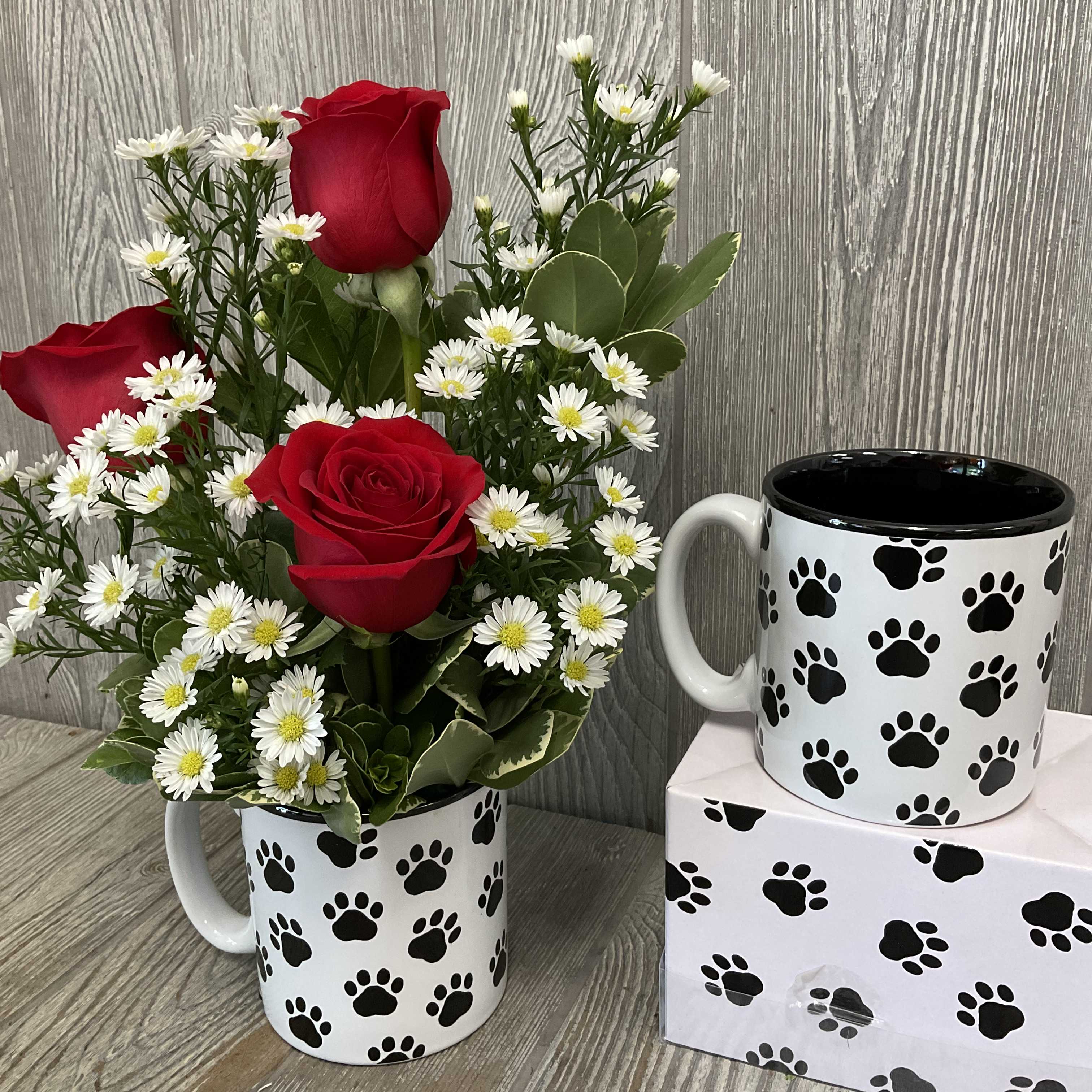 Red roses and white daisy flowers arranged in a paw-print mug