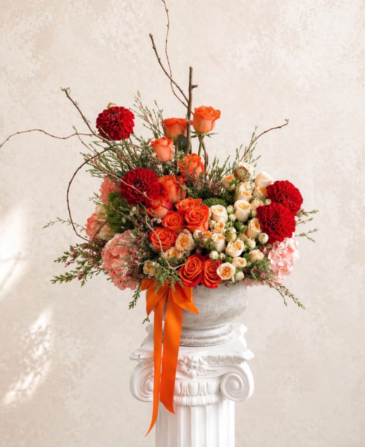 Orange and red rose arrangement in a white urn with an orange ribbon
