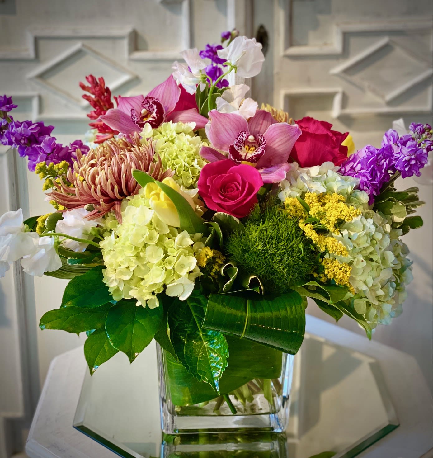 Colorful mixed bouquet in a clear glass vase with roses and orchids