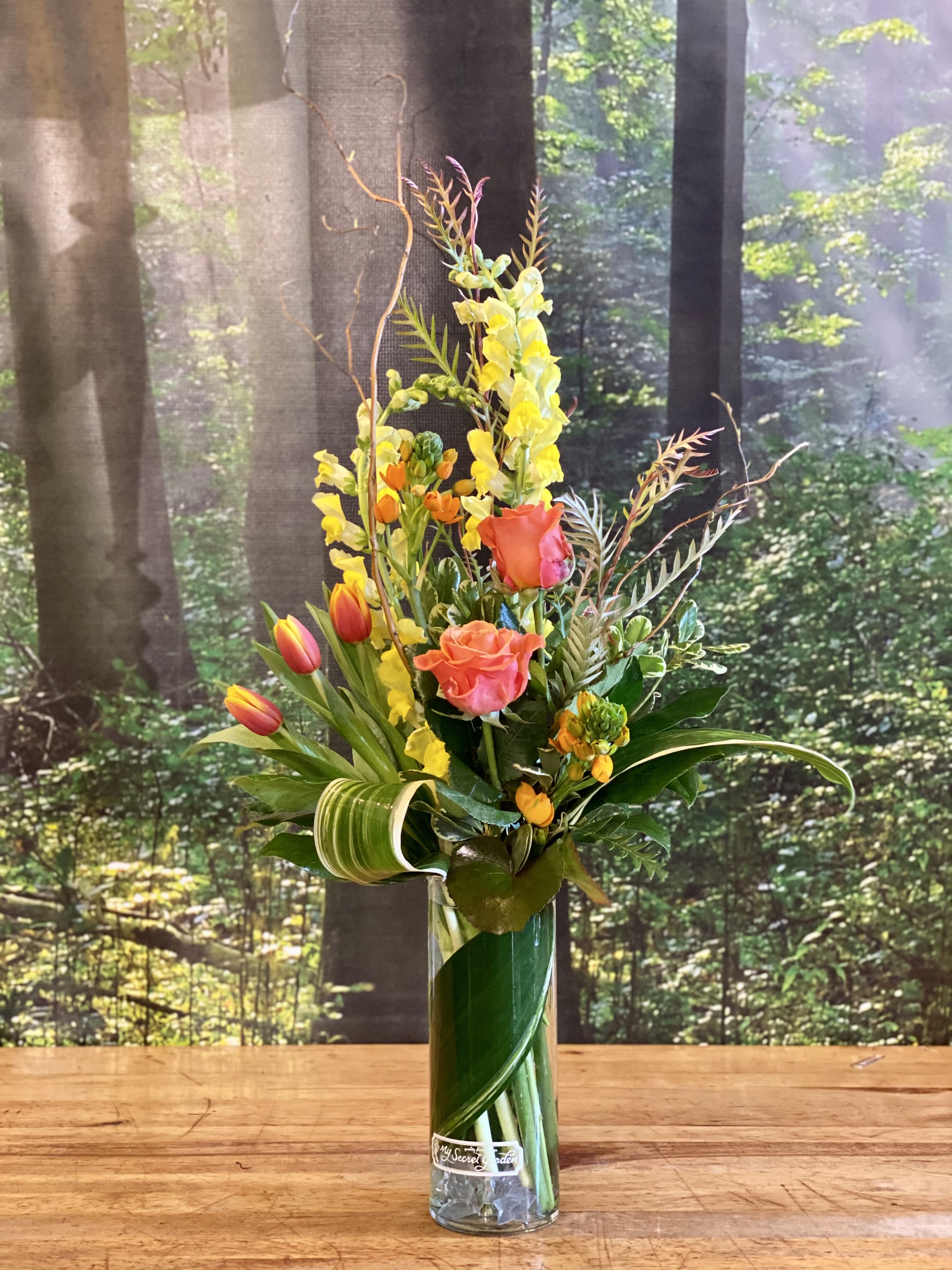 Spring Sunrise - Send Spring Sunshine! Orange, Yellow and Green flowers in a naturalistic modern and linear design create a stunning gift during the spring season. Includes daffodils, roses, tulips and fresh spring blooming branches. 