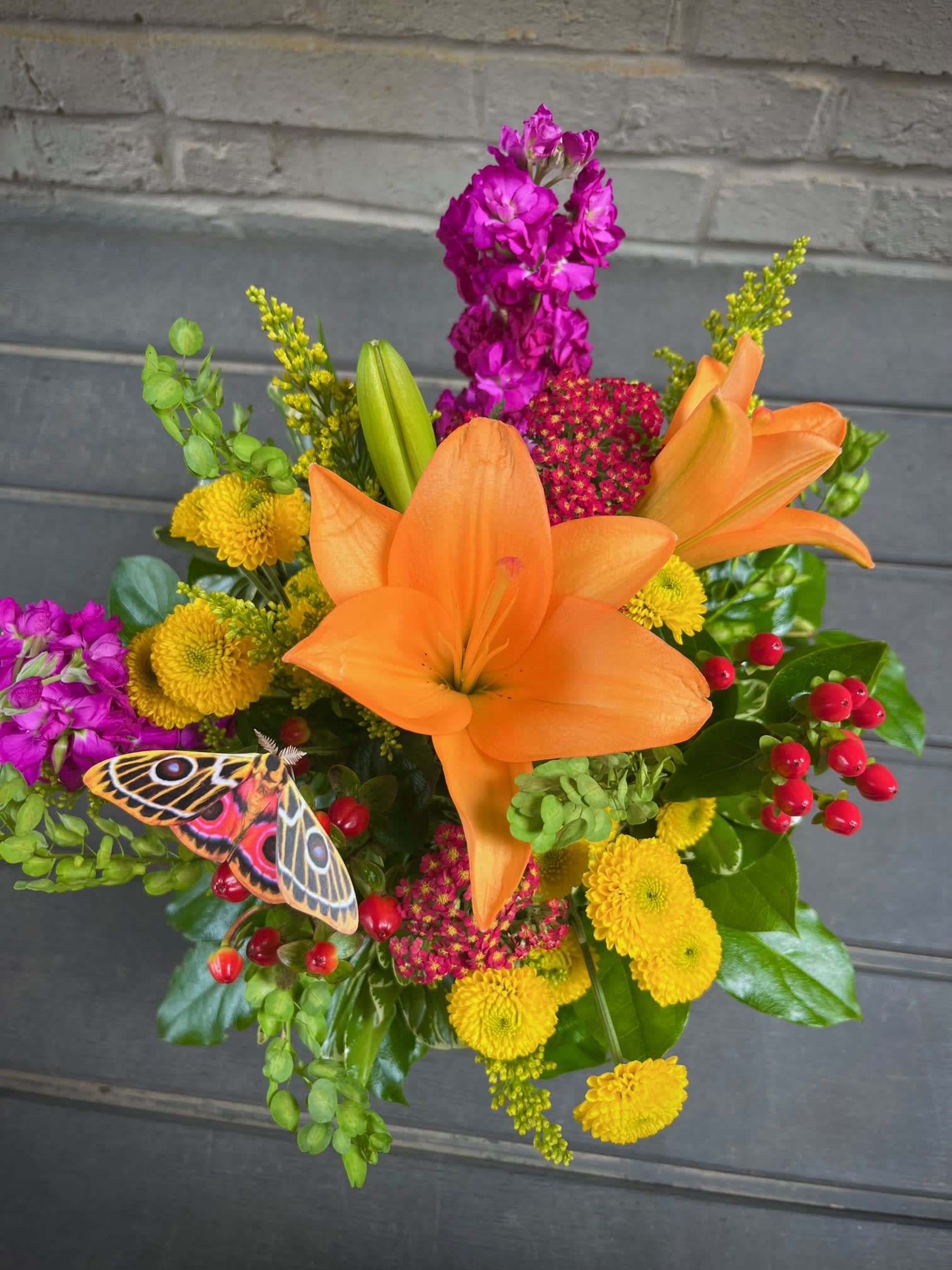 Bouquet of orange lilies, yellow mums, and purple flowers with a butterfly accent