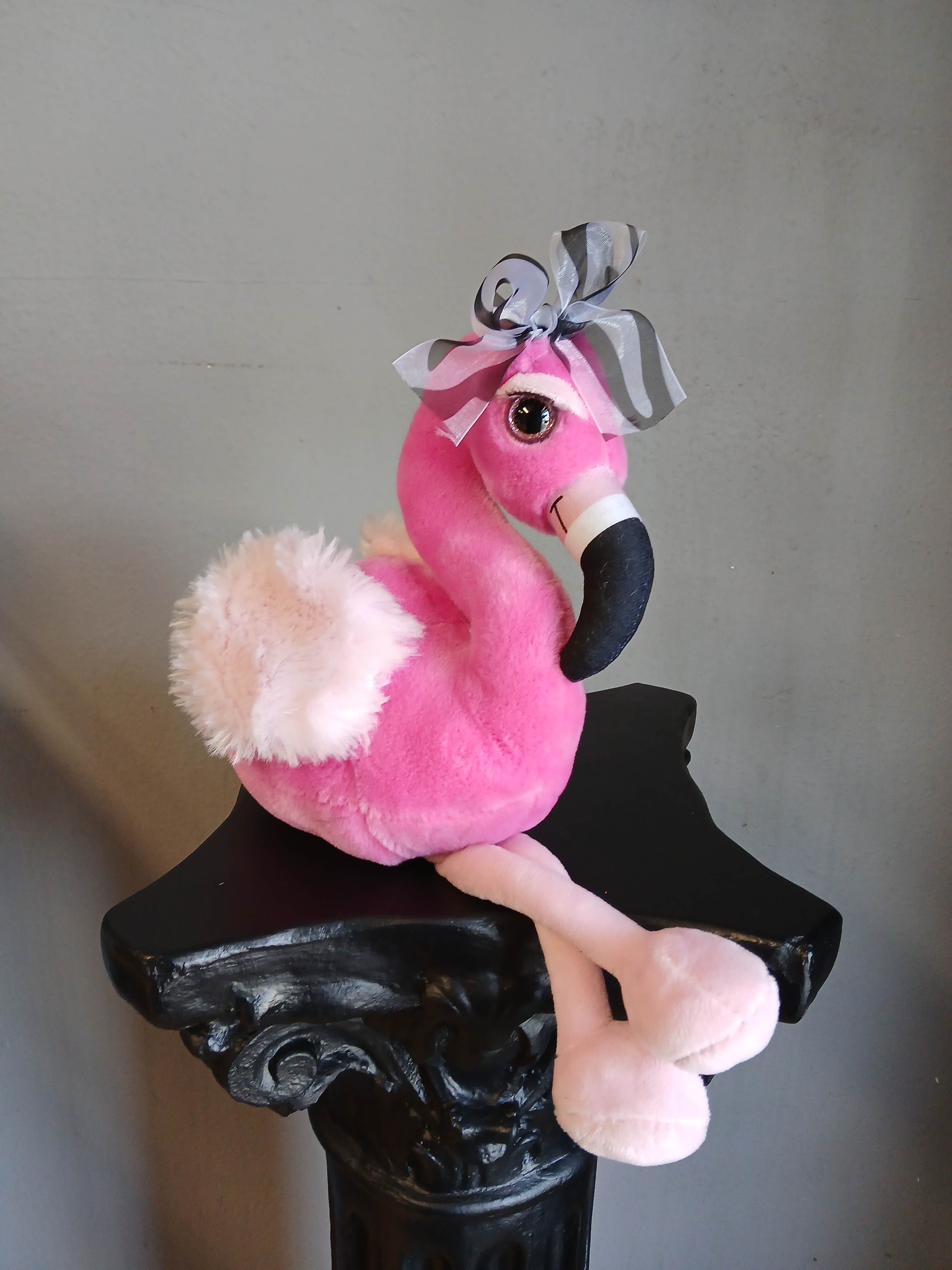 Pink plush flamingo with a striped bow sitting on a black pedestal