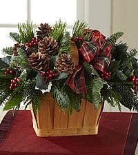 Holiday arrangement with pinecones, berries, and a plaid bow in a wooden basket