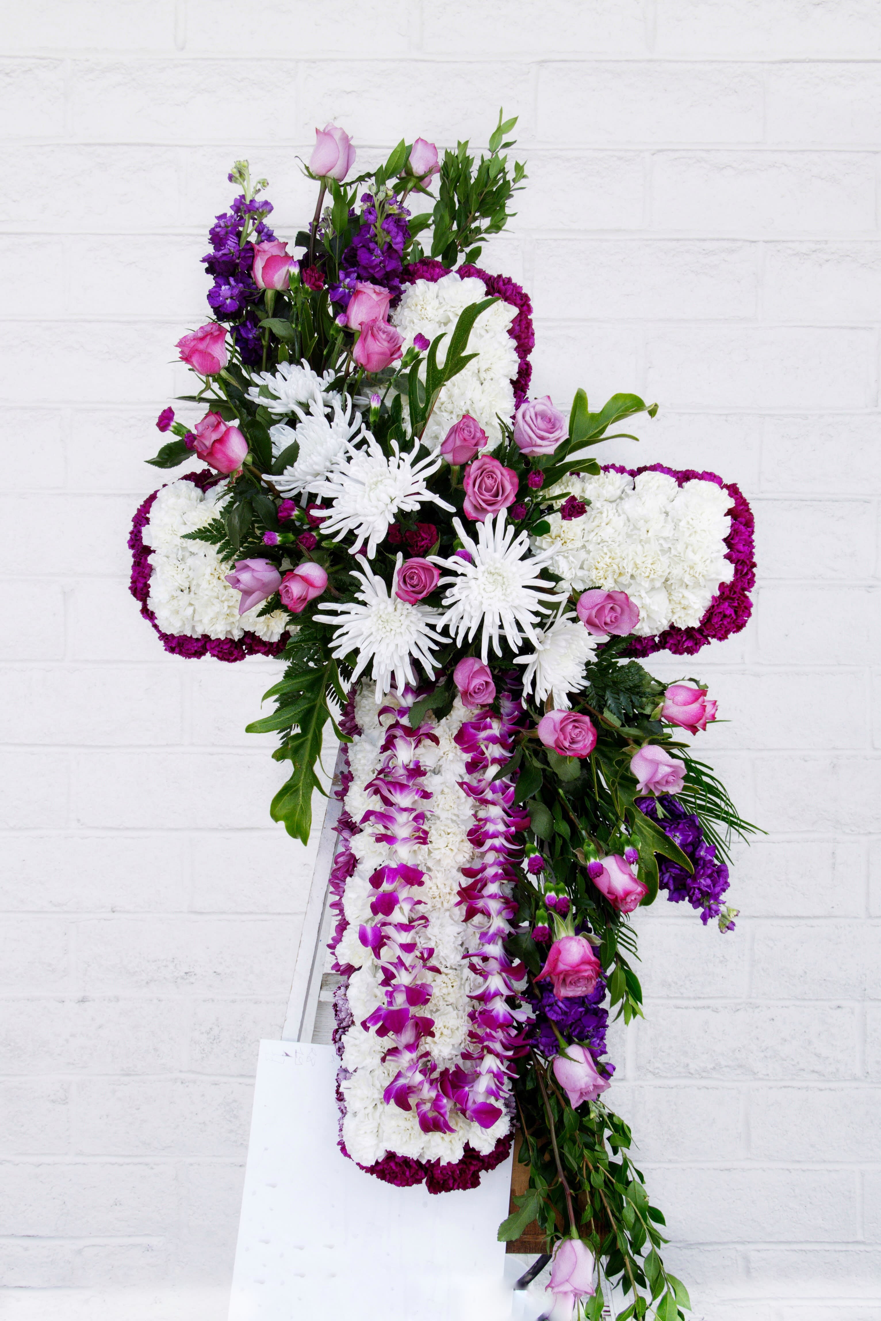 Cross-shaped floral tribute with pink roses, white chrysanthemums, and purple orchids
