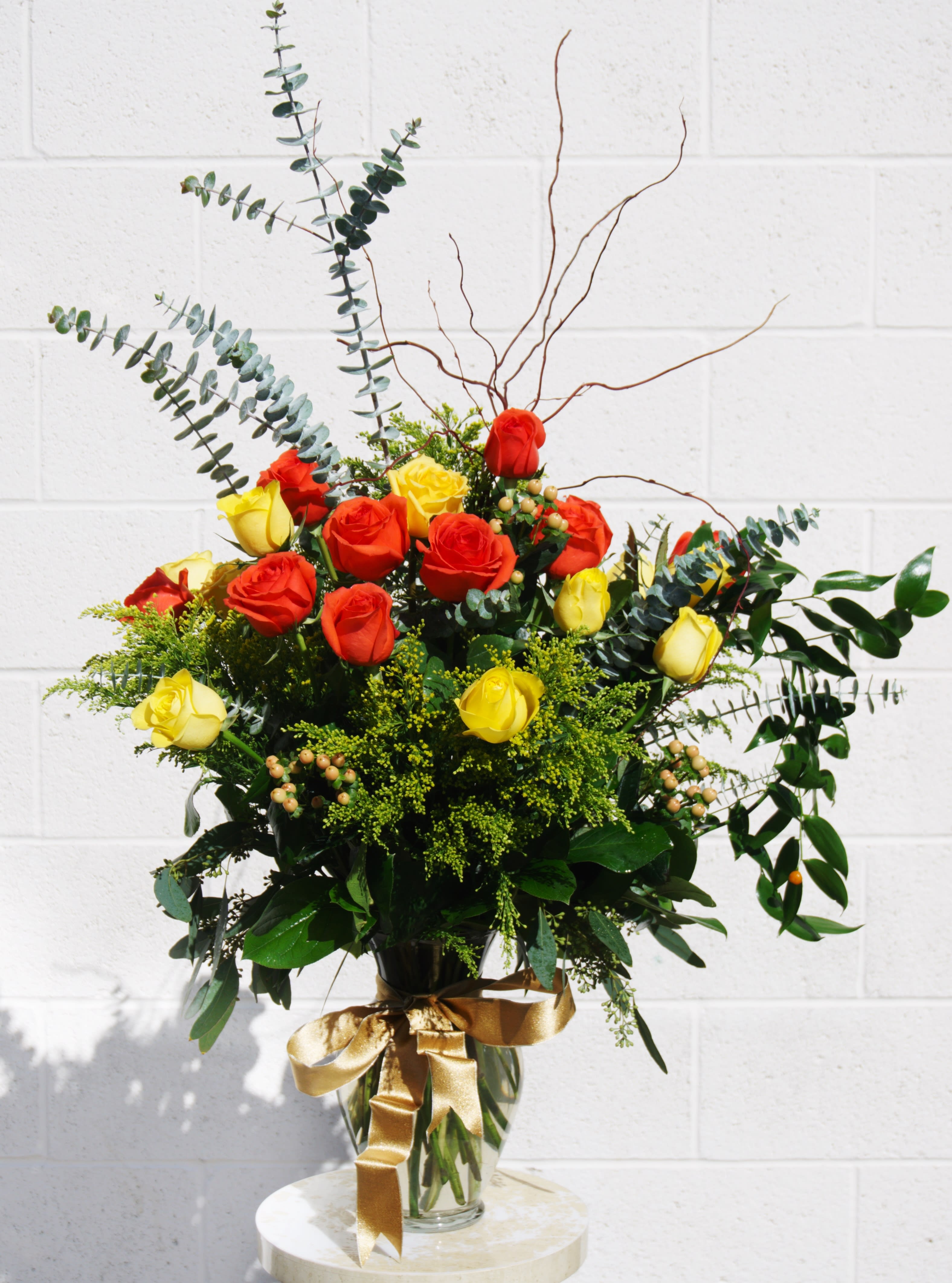 Bouquet of red and yellow roses in a glass vase with a gold ribbon