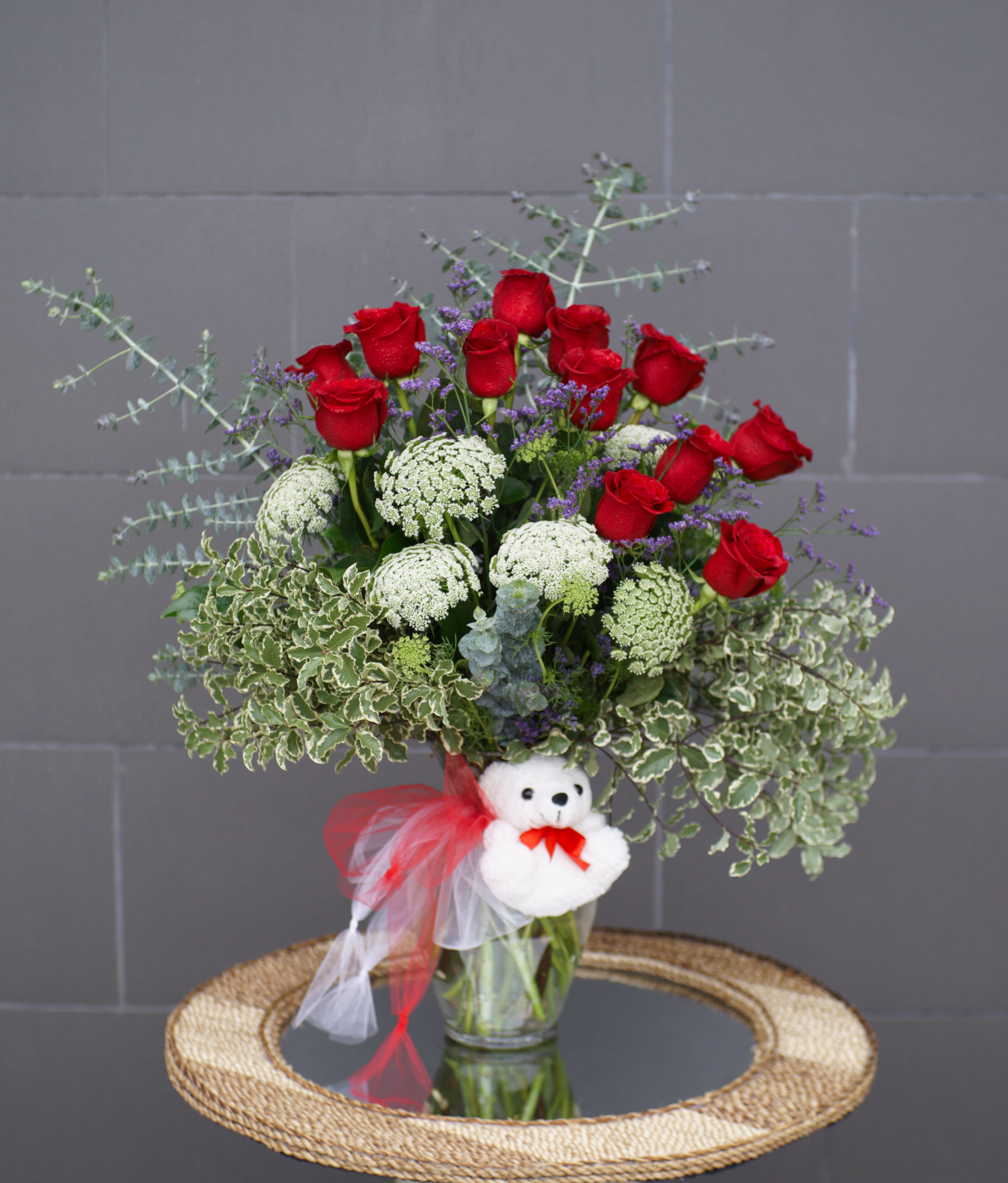 Bouquet of red roses with white filler flowers in a glass vase, decorated with a teddy bear