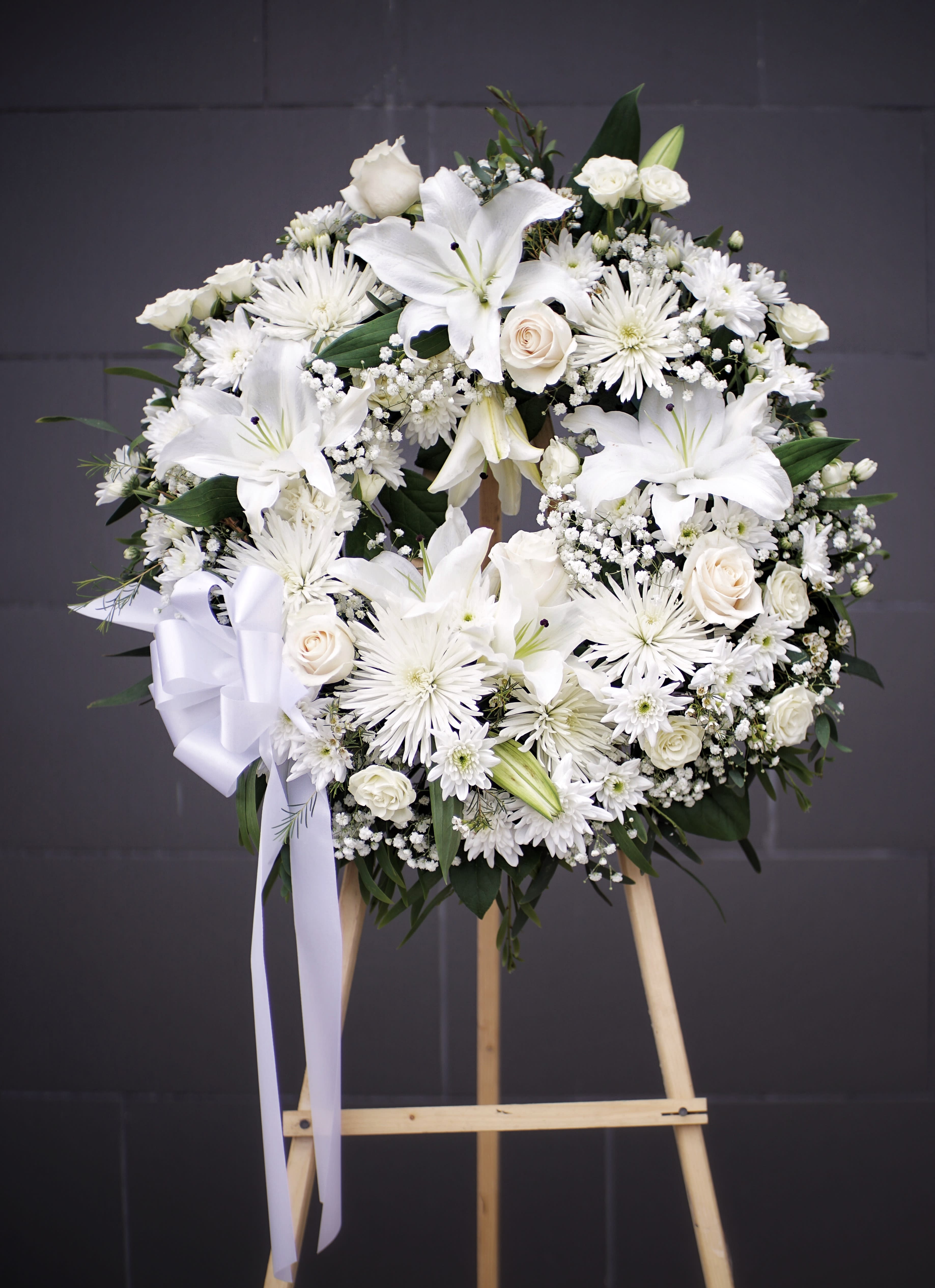White floral wreath on a wooden easel with a ribbon bow