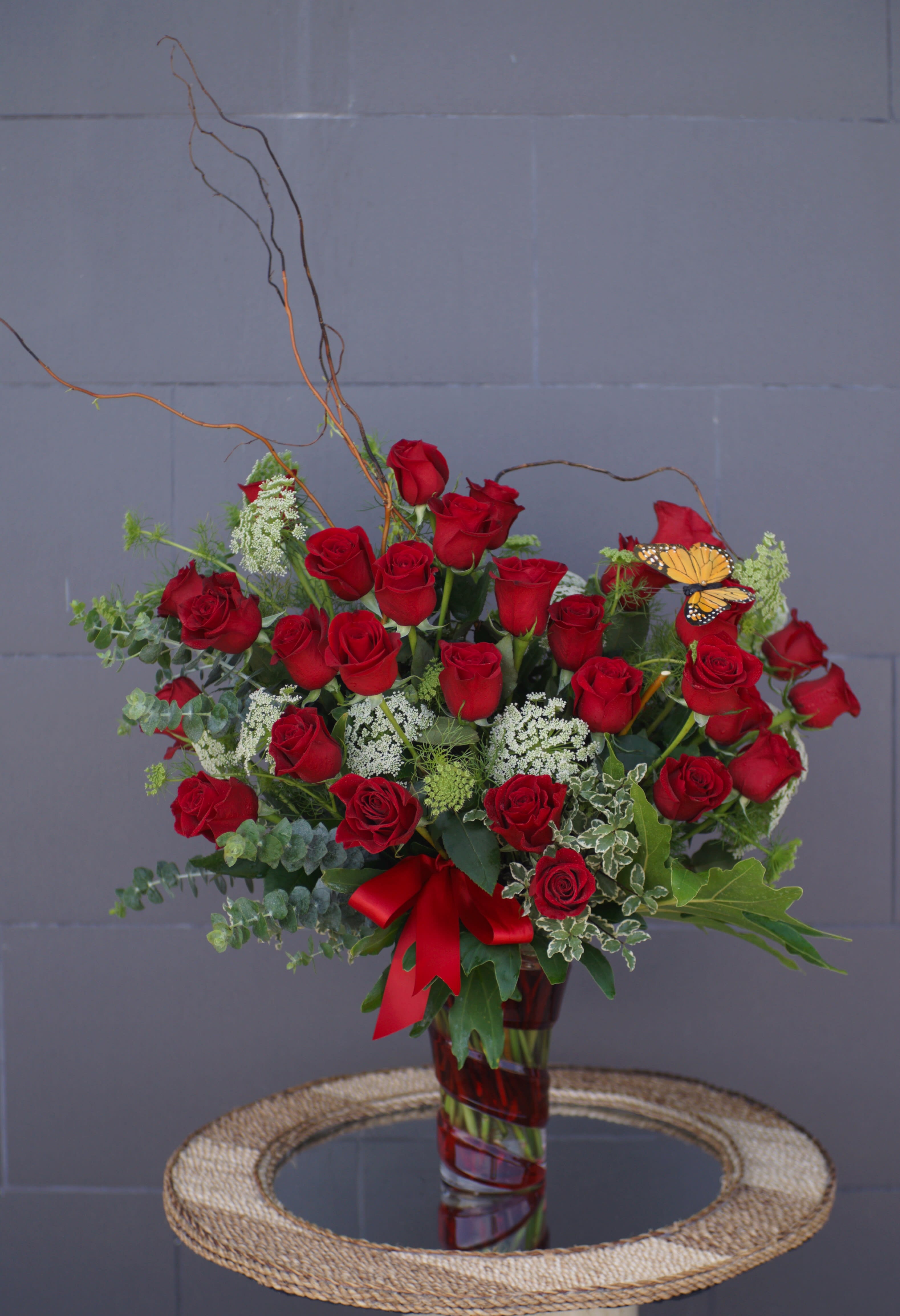 Red roses arranged in a glass vase with a red ribbon and butterfly accent
