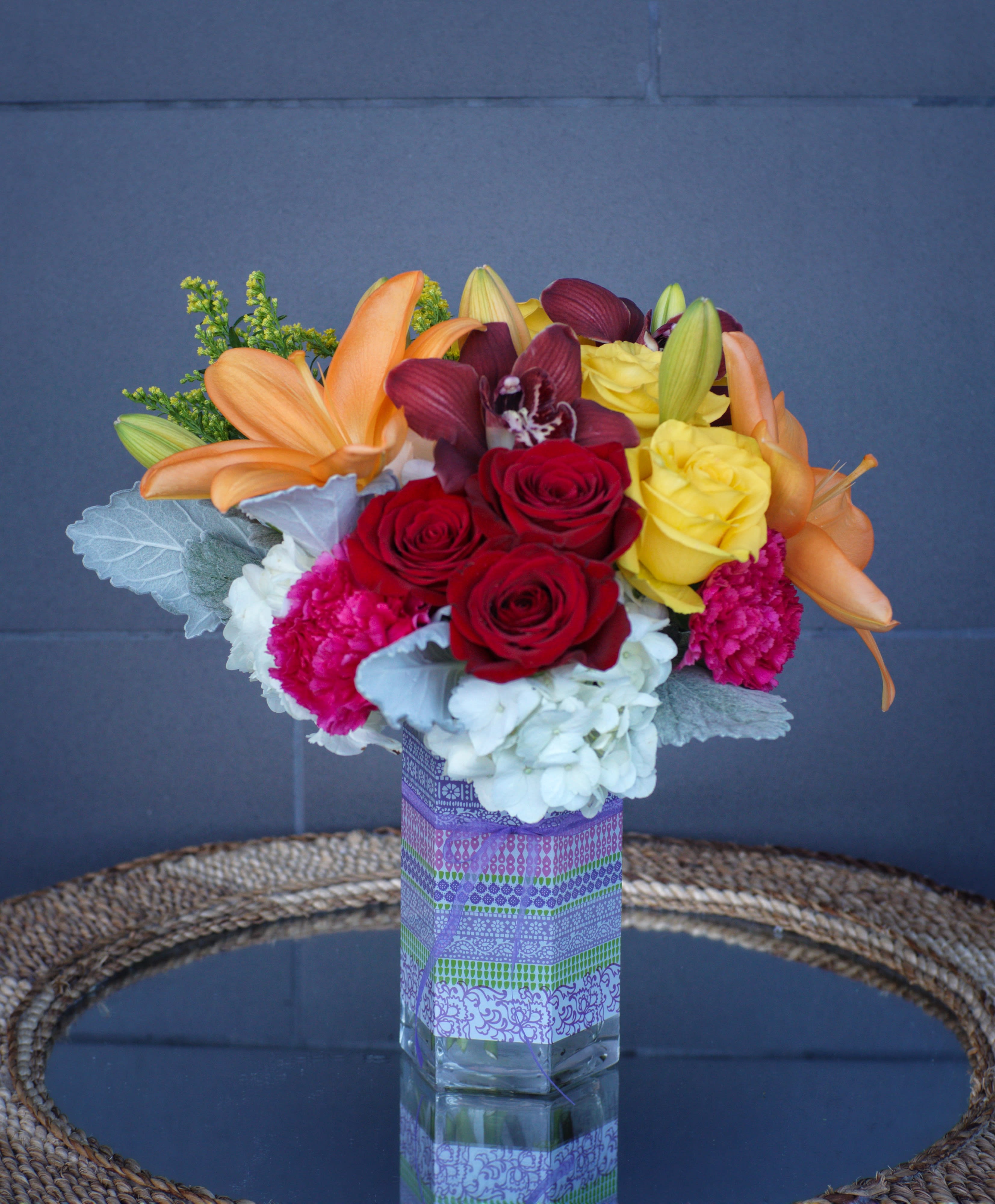 Mixed bouquet of roses, lilies, orchids, and carnations in a glass vase