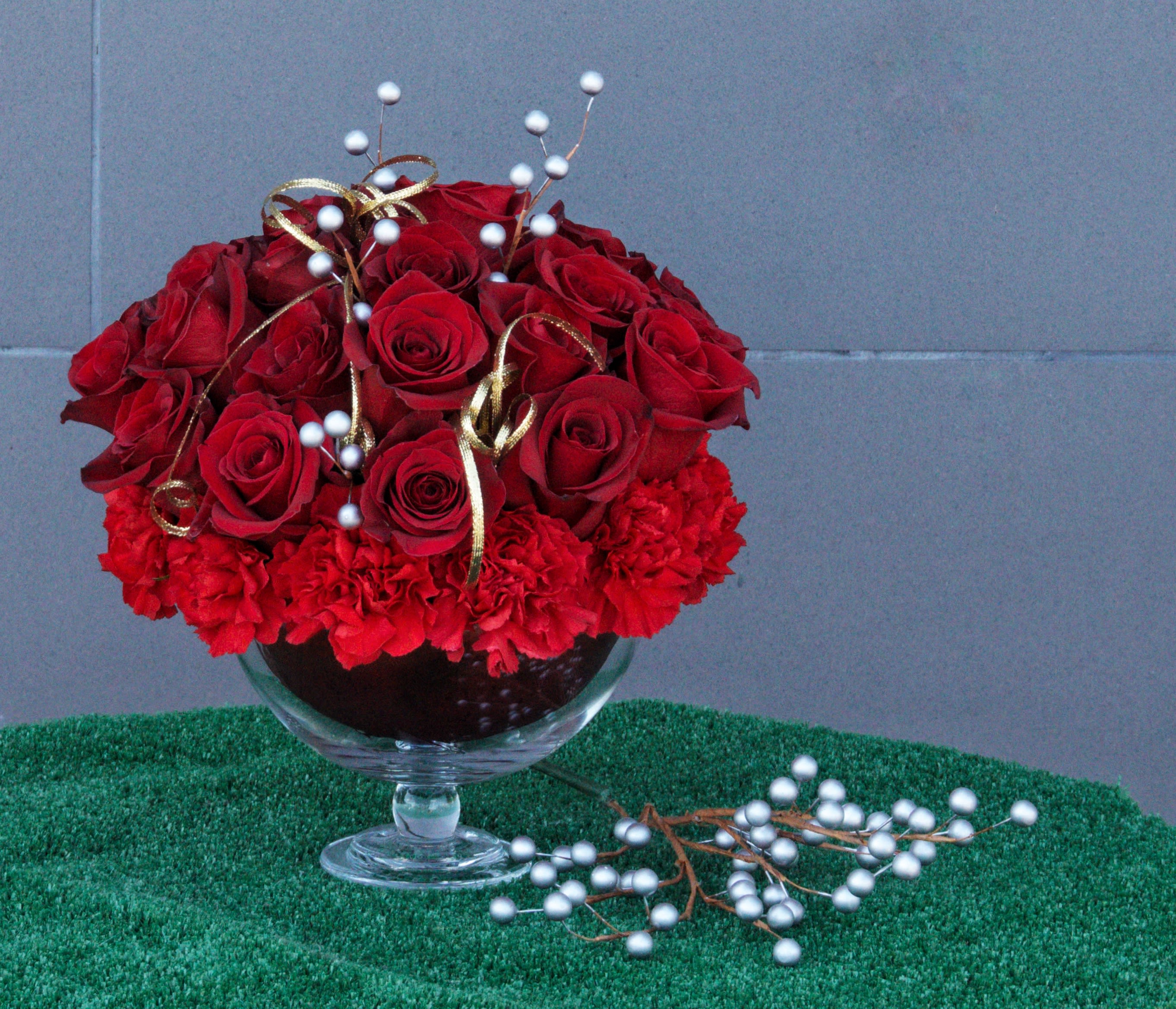 Red roses and carnations in a glass compote with gold ribbon and white berry picks