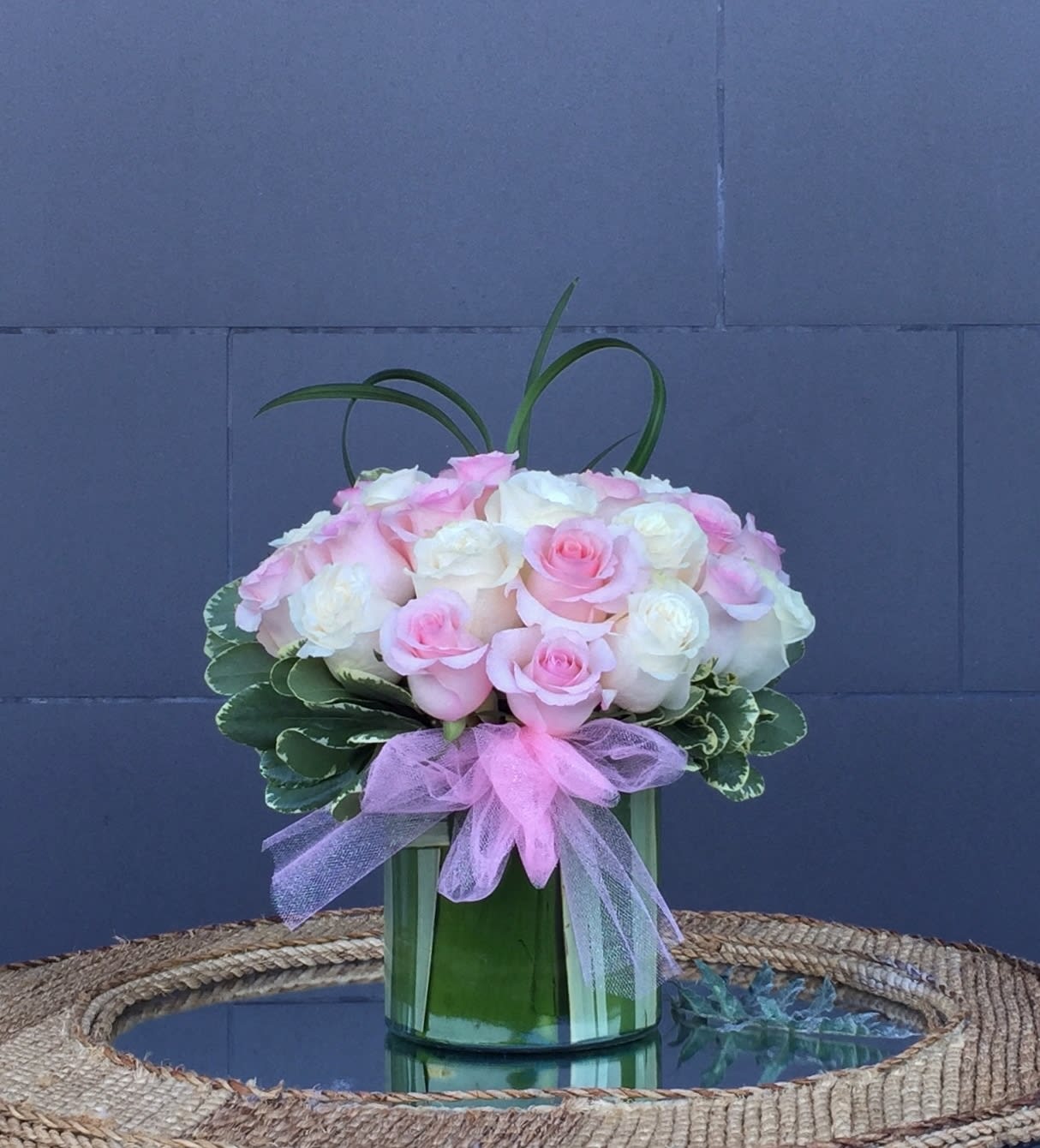 Pink and white roses arranged in a green glass vase with a pink ribbon.