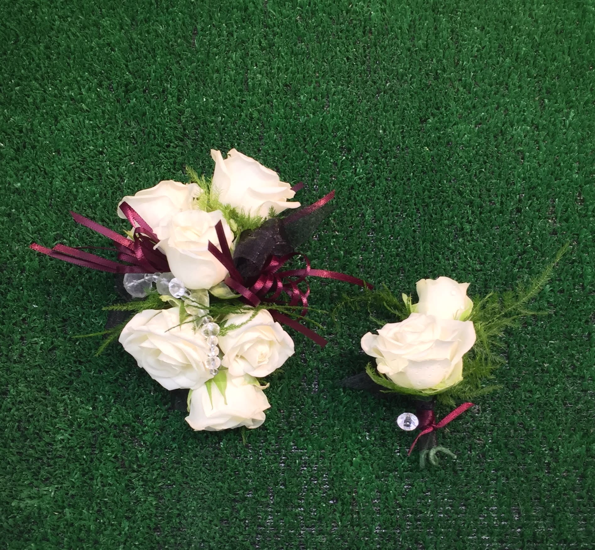 White rose boutonnieres with burgundy ribbon on green turf