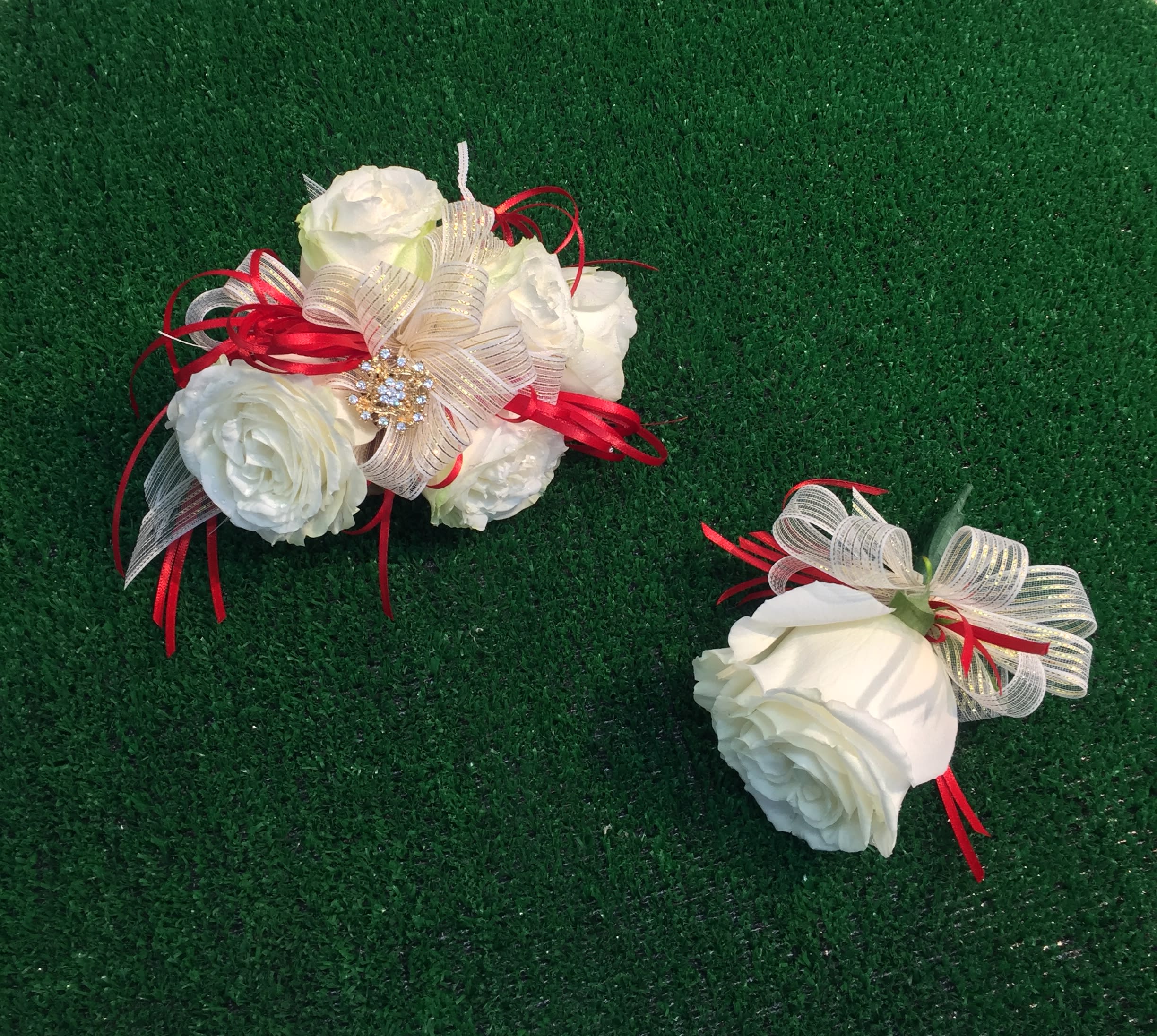 Two white rose corsages with red and gold ribbon accents