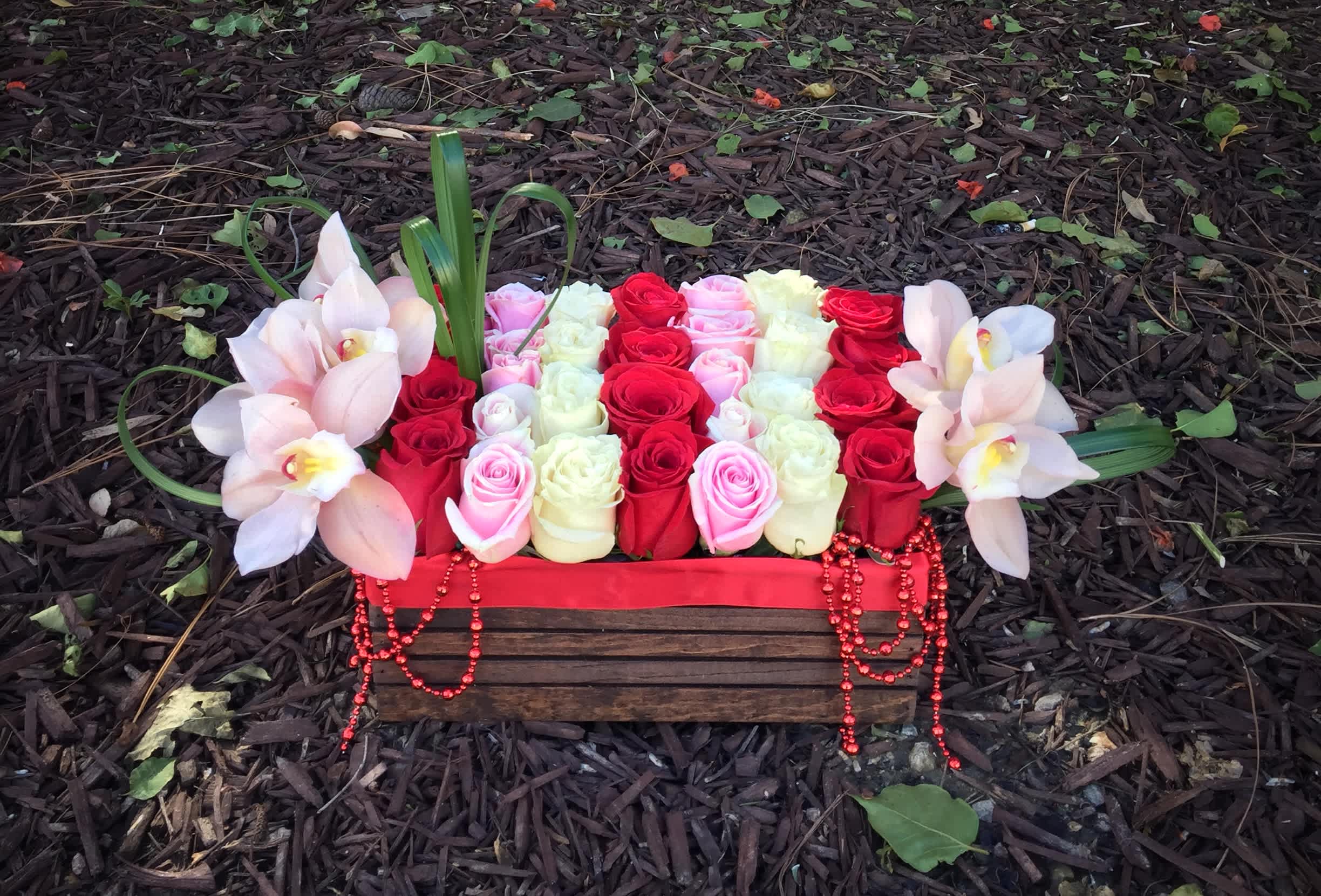 Rectangular floral arrangement with red, pink, and white roses and pale orchids in a wooden box