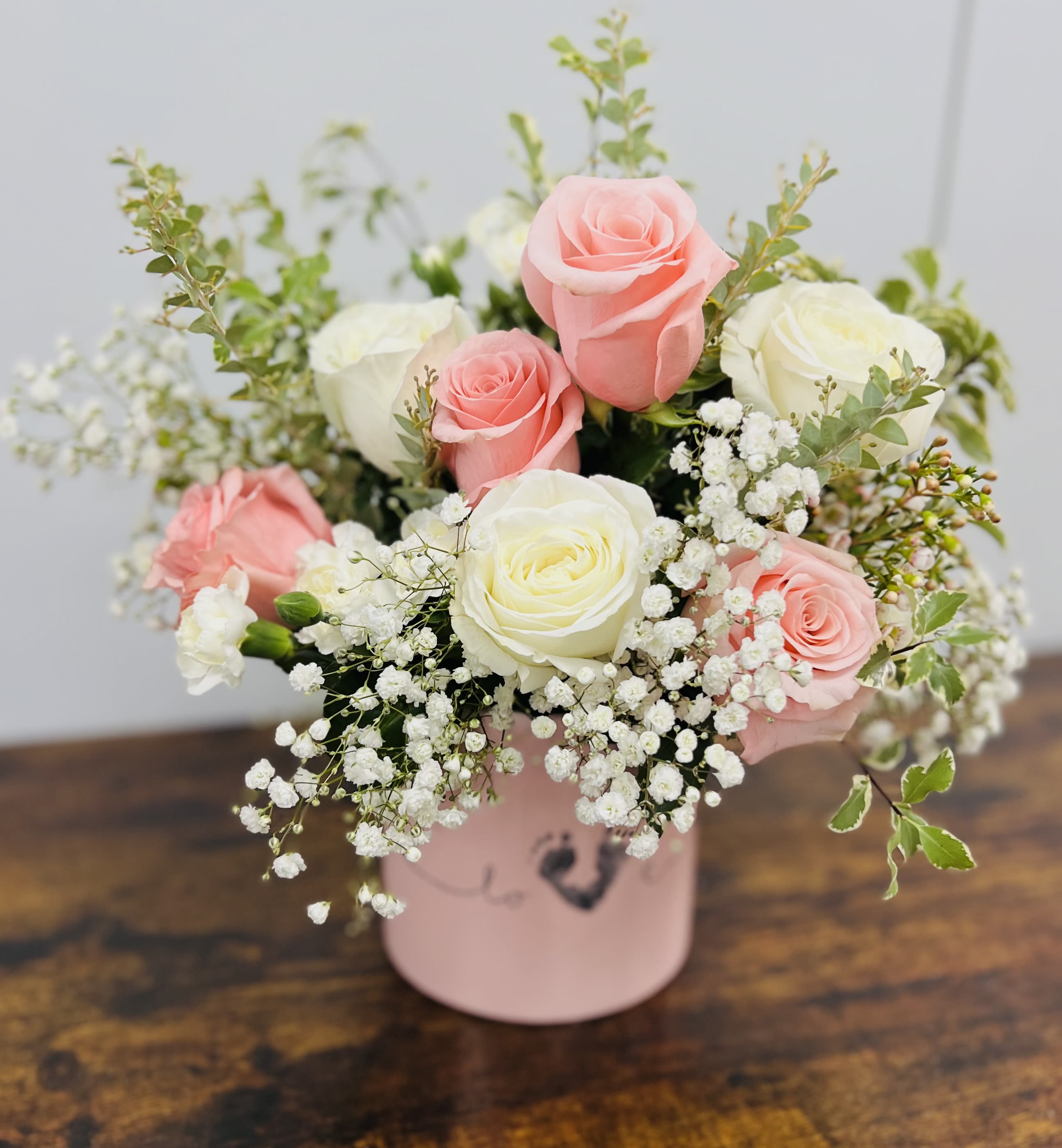 Pink and white roses arranged in a pink box with baby's breath
