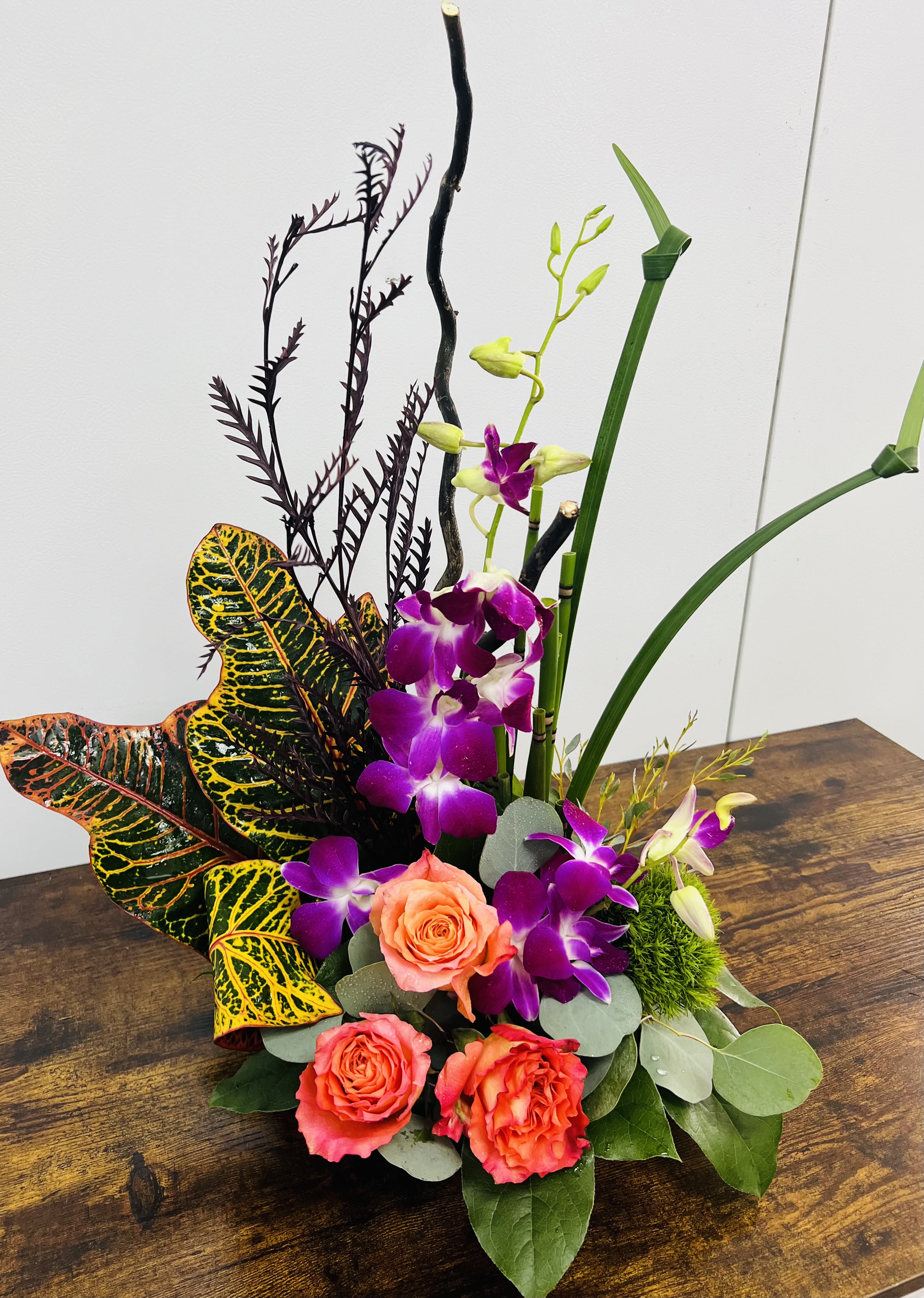 Tropical floral arrangement with purple orchids and coral roses