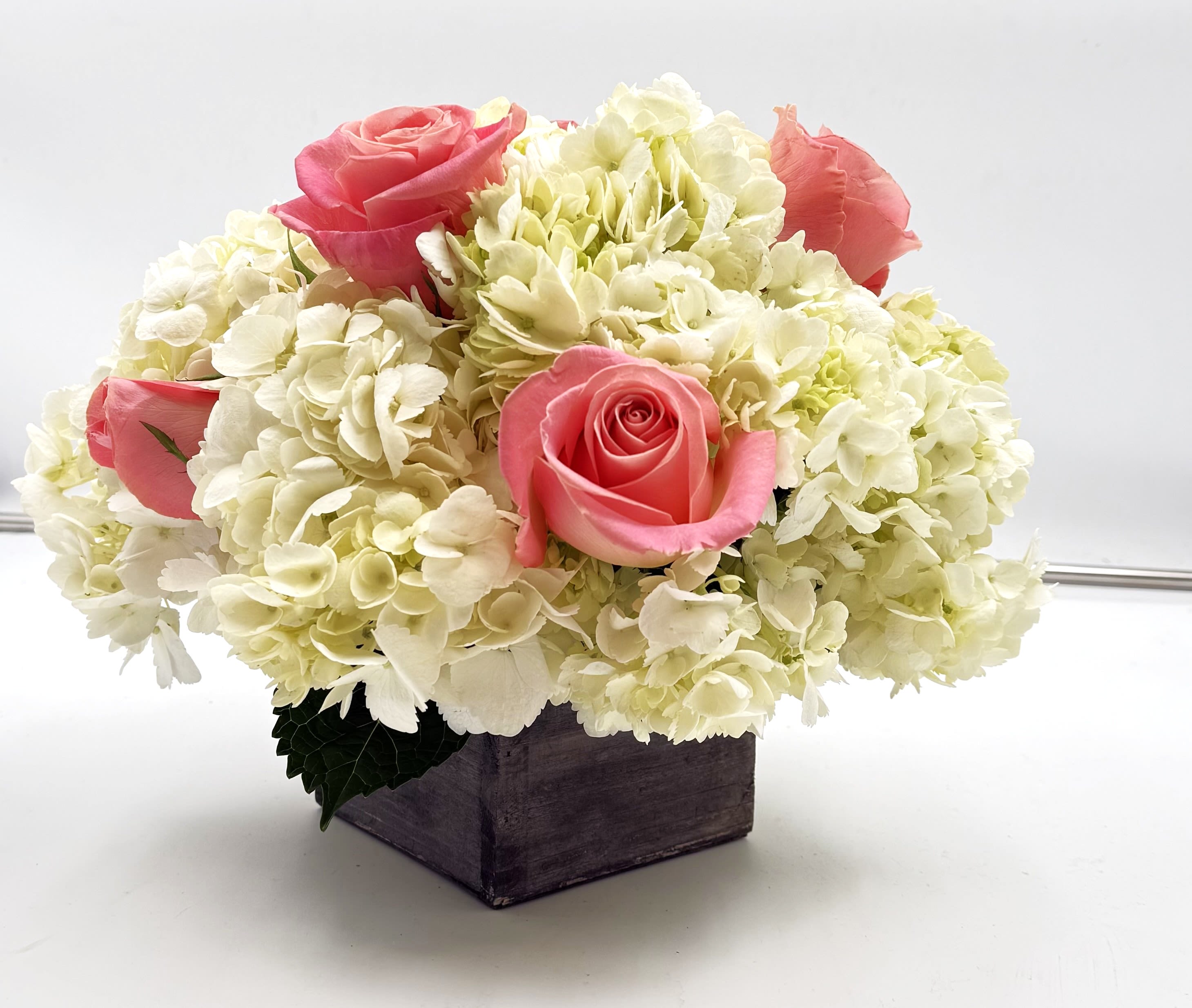 Pink roses arranged with white hydrangeas in a wooden box