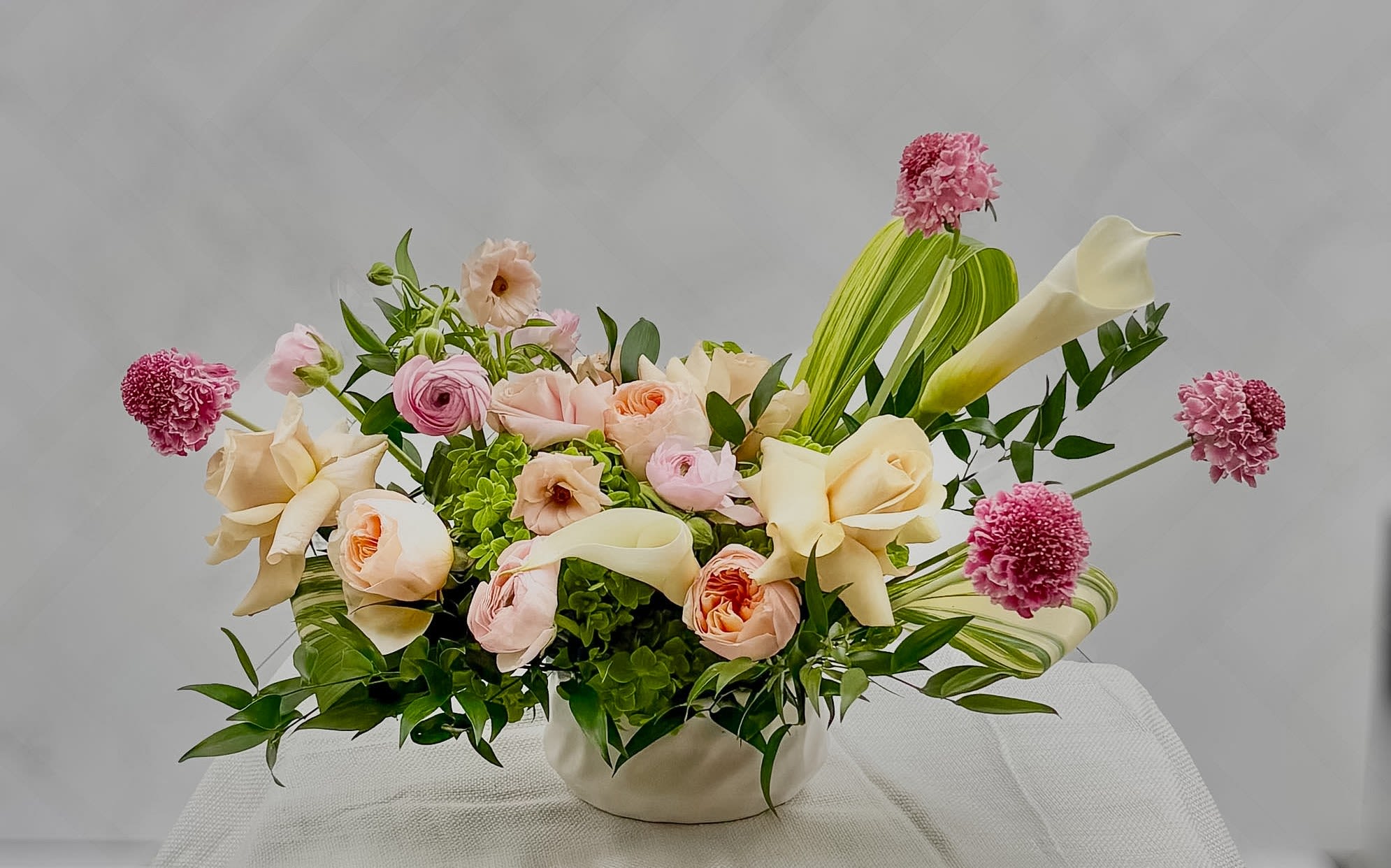 CANVAS IN BLOOM - This abstract arrangement is a brand new design. Designed exclusively by one of our in house designers, Jessica.  Features, quicksand roses, garden Roses, Ranunculus, cala lily's, and scabiosa. This is a true Fine Flowers signature creation.