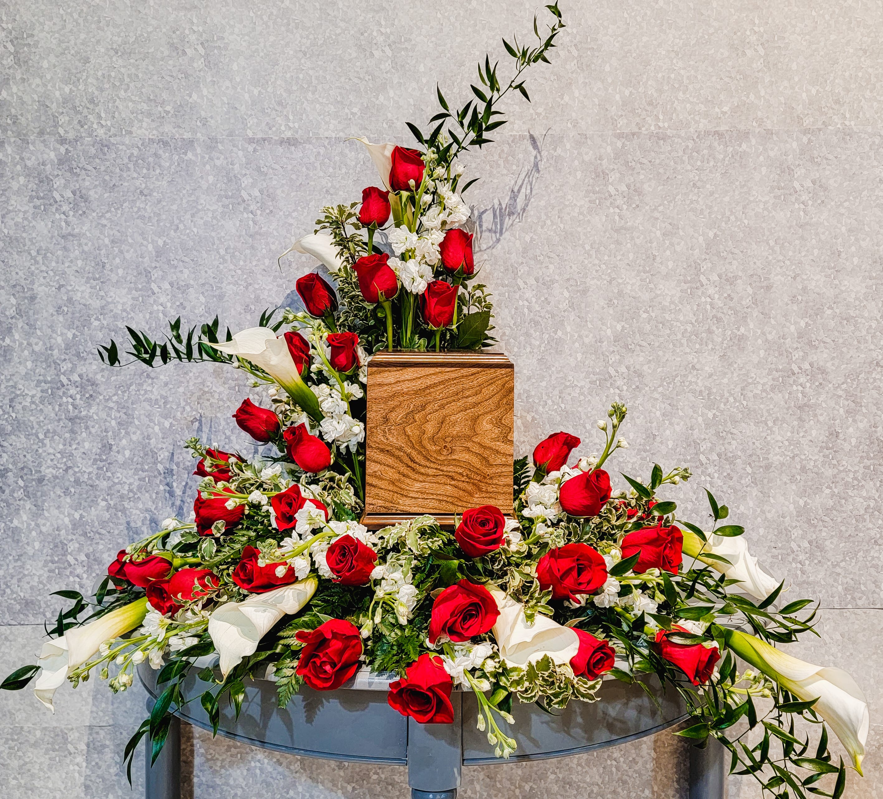 Large floral arrangement with red roses and white calla lilies around a wooden urn