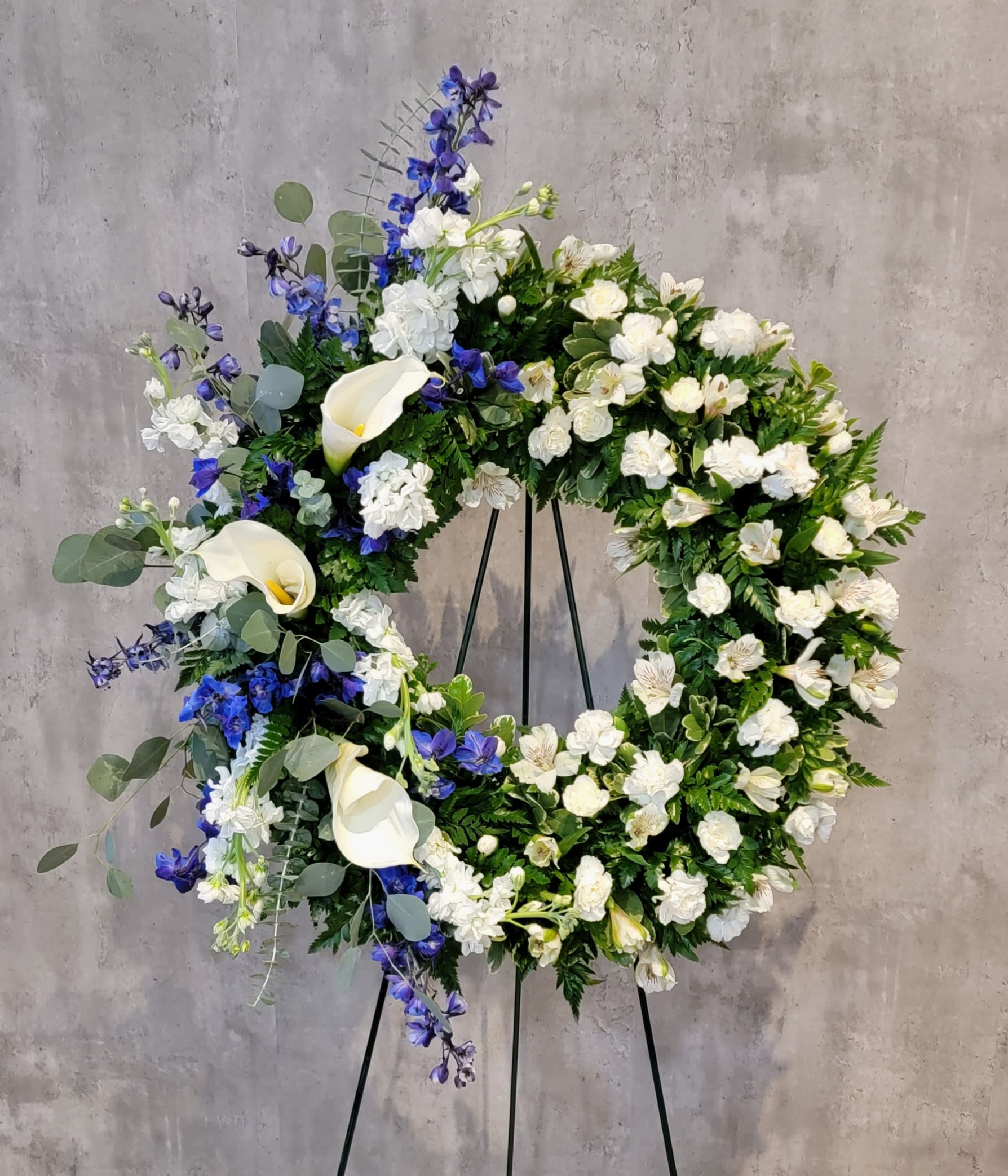 Large floral wreath with white calla lilies and blue flowers on a stand
