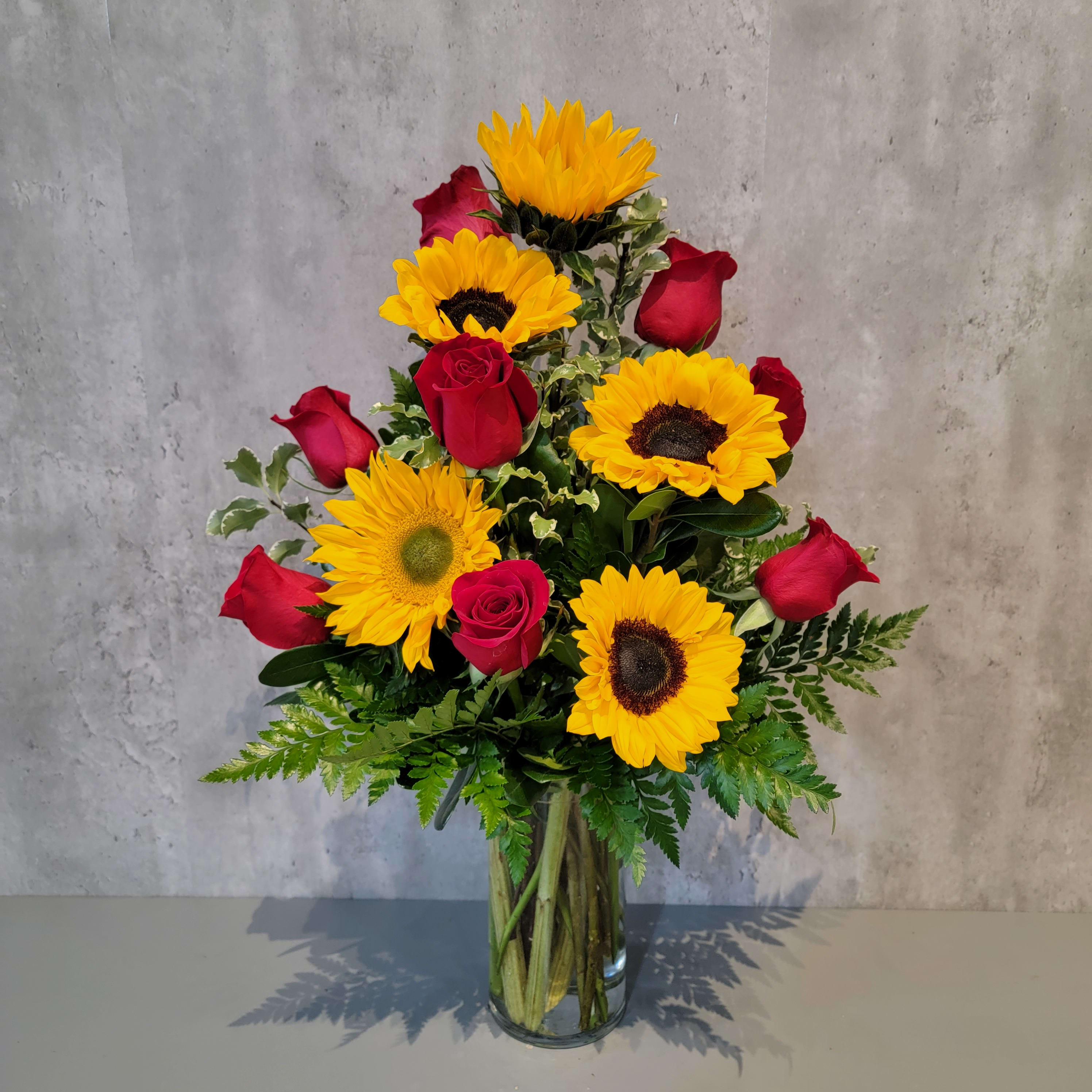 Bouquet of red roses and yellow sunflowers in a clear glass vase