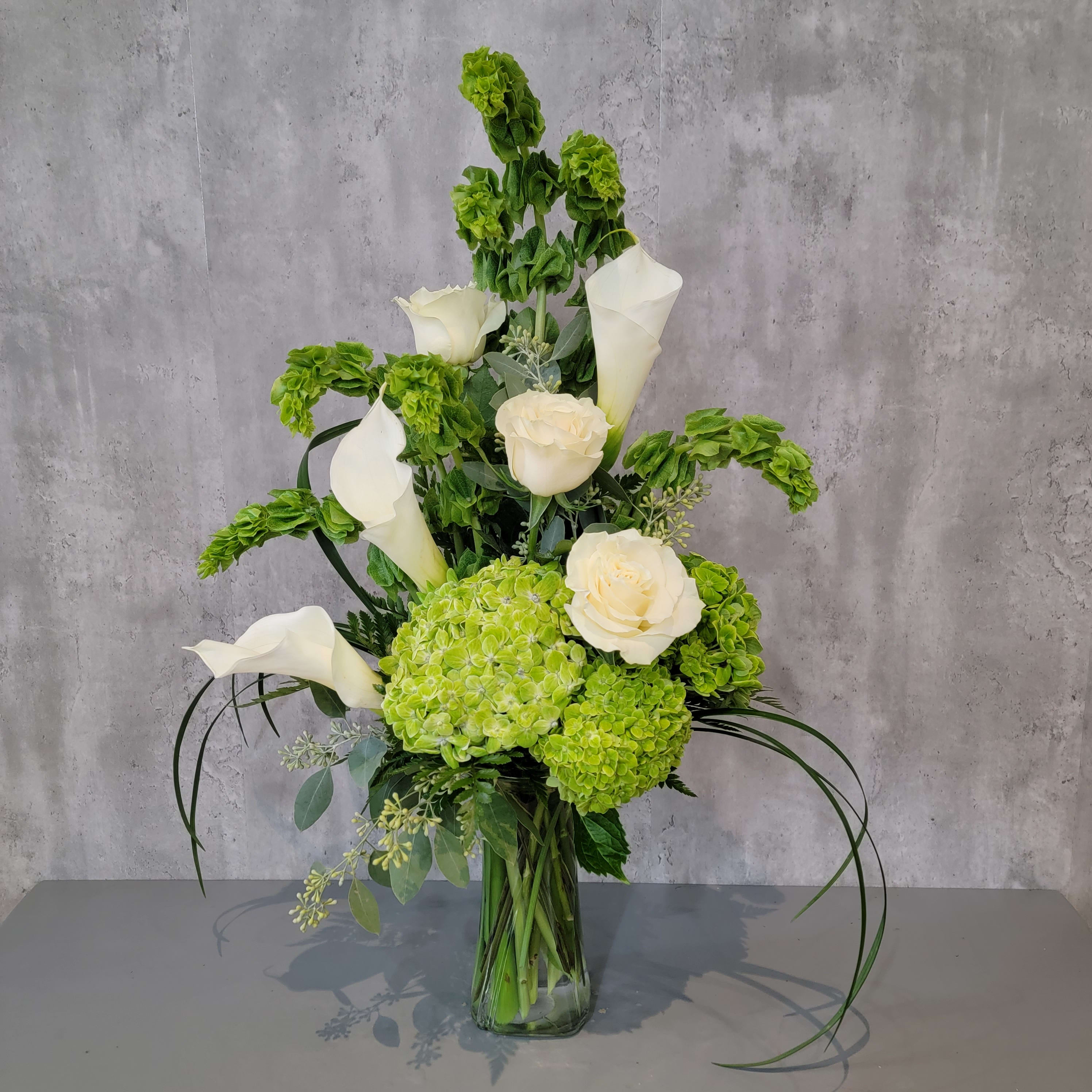 Green hydrangeas and white calla lilies in a glass vase