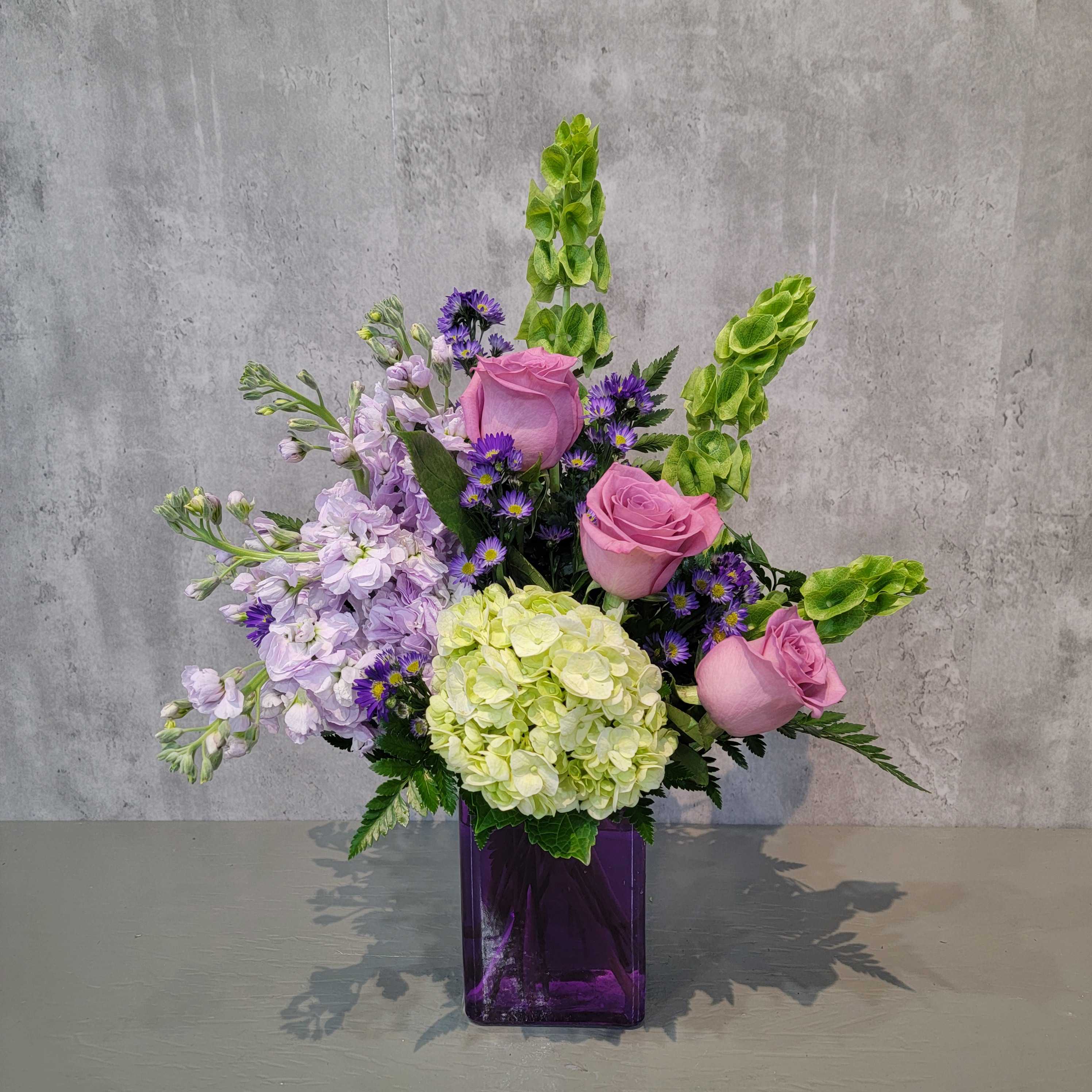 Purple Passion - Introducing "Purple Passion," a captivating floral arrangement in a striking purple vase, perfect for any occasion. This stunning bouquet features elegant purple roses, lush green hydrangea, charming Bells of Ireland, and delicate purple monte casino, creating a harmonious and vibrant display.  Your reliable Albuquerque florist, Flowers by Zach-Low, is locally owned and operated, ready to deliver fresh flowers throughout Albuquerque. Since 1993, we have passionately served the Albuquerque area, striving to be the best florist in town. We offer same-day flower delivery, ensuring your loved ones receive their beautiful arrangements promptly. Trust Flowers by Zach-Low to bring joy and beauty to your special moments.