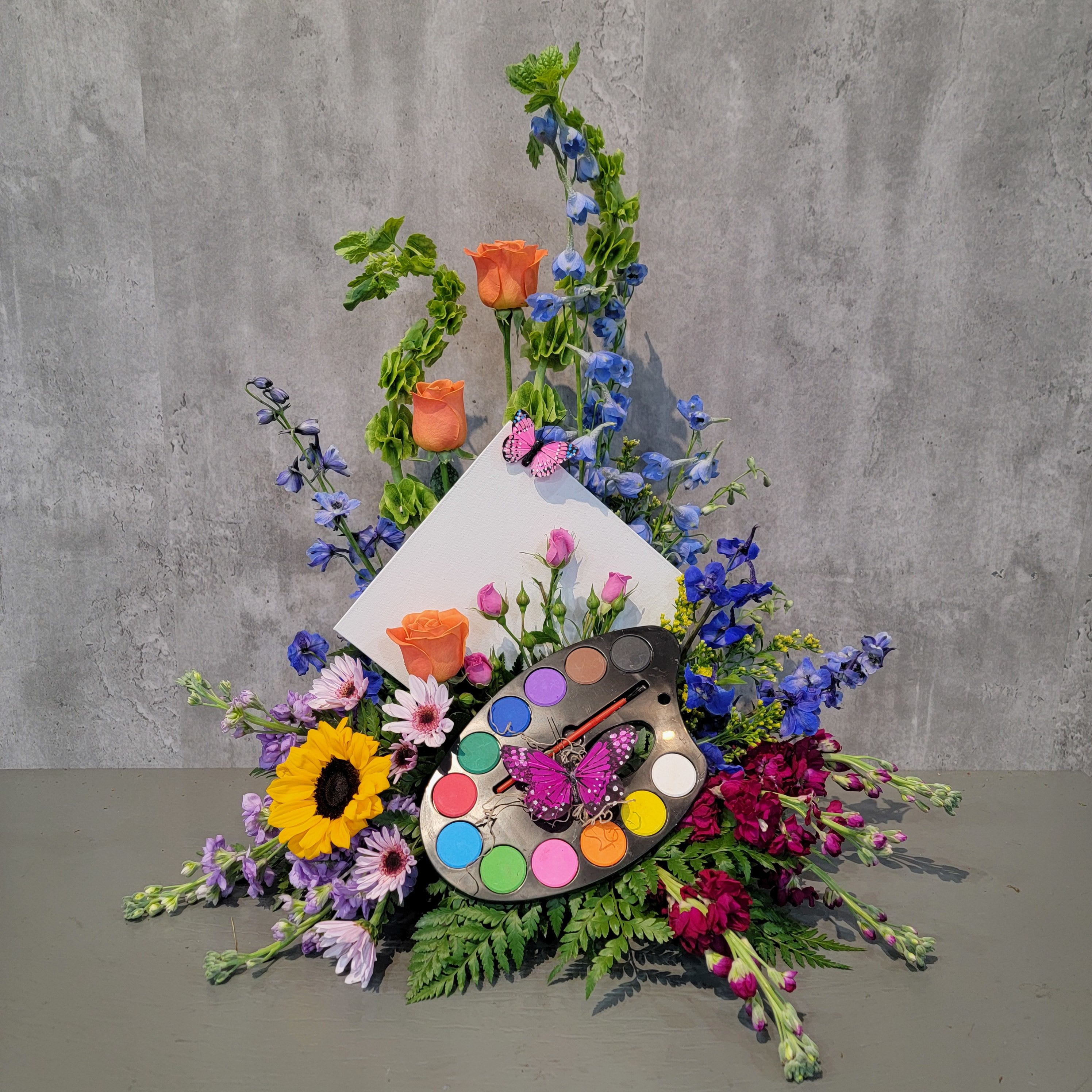Colorful floral arrangement with roses, sunflowers, and a paint palette centerpiece
