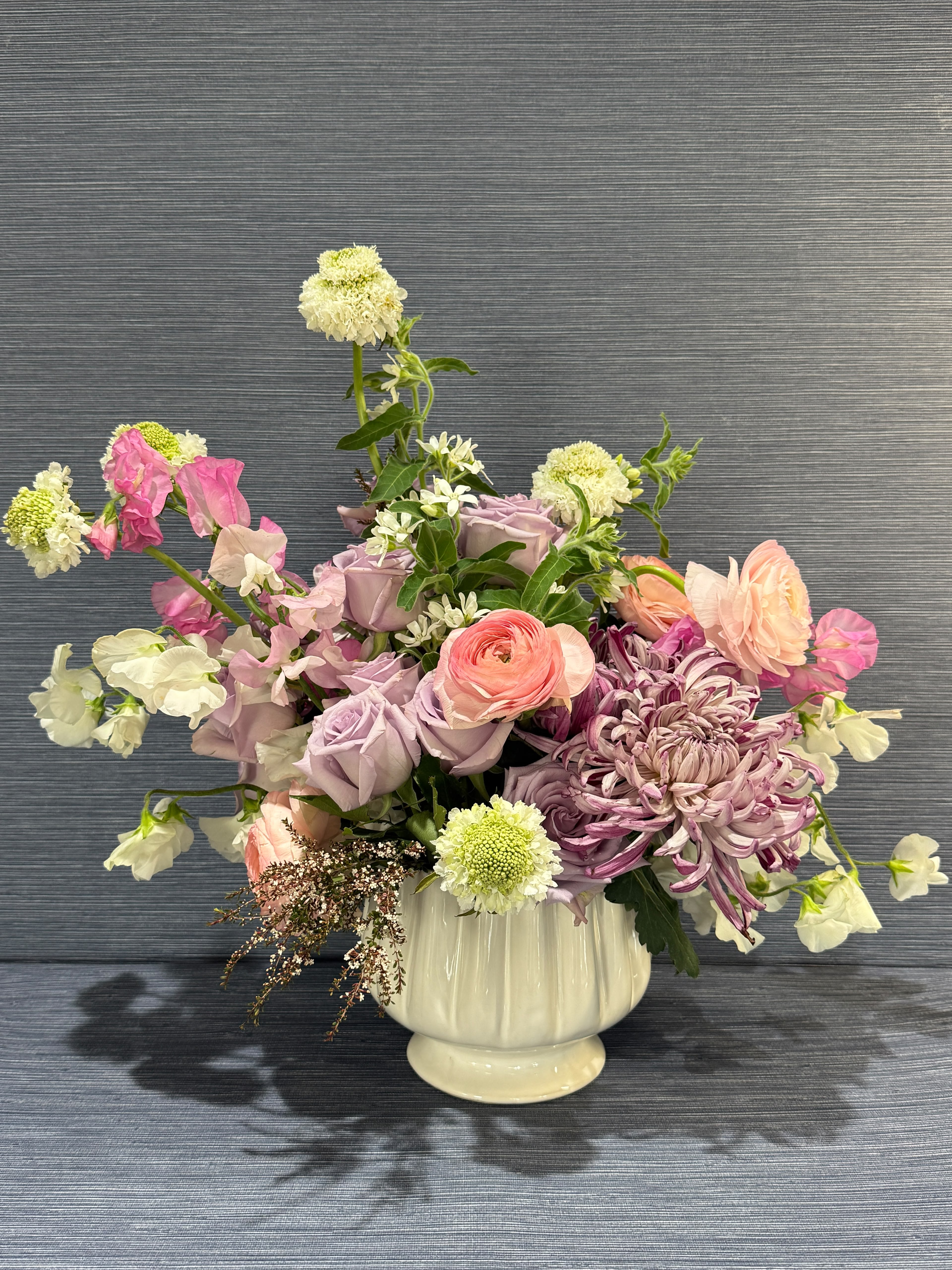 Blush &amp; Bloom - A soft, springlike blend of pinks, purples, whites, and fresh greens makes this floral arrangement a heartfelt choice for birthdays, anniversaries, or a thoughtful thank-you. The garden-style mix-centered on layered roses and a prominent blush ranunculus or spider chrysanthemum-reads romantic and cheerful, the kind of bouquet that makes the person you're thinking of feel noticed and genuinely celebrated.