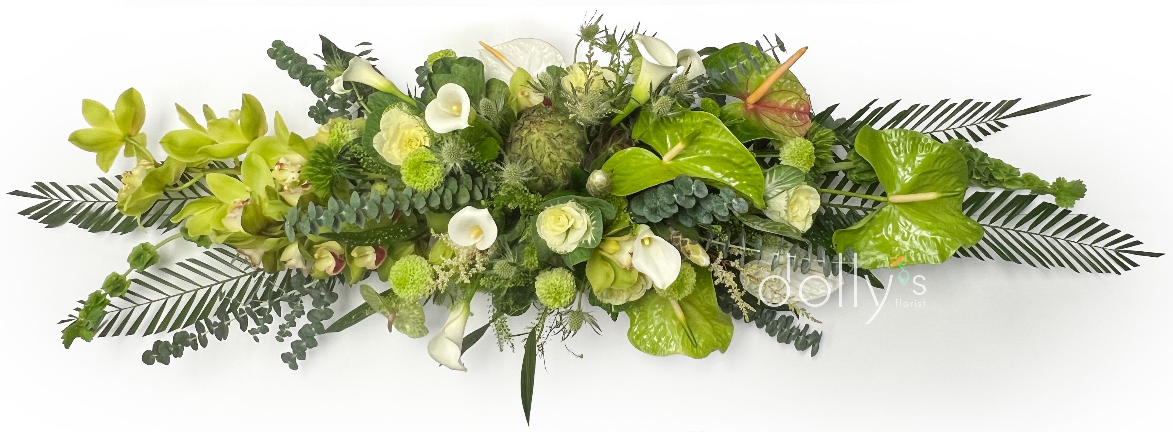 The Green Goddess - A long, low flower arrangement built in a rectangular wooden box, The Green Goddess is a serene, contemporary centerpiece perfect for a wedding table, sympathy tribute, housewarming, or a refined everyday display. The horizontal, sculptural silhouette and predominantly green-and-white palette create a calm, elegant impression that will make the person you're sending it to feel seen and soothed.  Layered textures of glossy foliage and sculptural green accents form a dense, living base, while white calla lilies and pale green orchids rise from the center for contrast and vertical interest. Small white blooms and rounded green elements add softness and rhythm across the composition, giving it an airy edge and a concentrated, lush middle-ideal for placement on long dining tables, reception desks, or mantel displays.  Designed to arrive ready to display in its wooden box, this low, sprawling design needs minimal care-keep it in a cool spot out of direct sun and refresh the water as needed to maintain freshness. Its modern, monochromatic look reads as both celebratory and quietly reverent, a thoughtful choice when you want someone to feel comforted, honored, or beautifully celebrated.