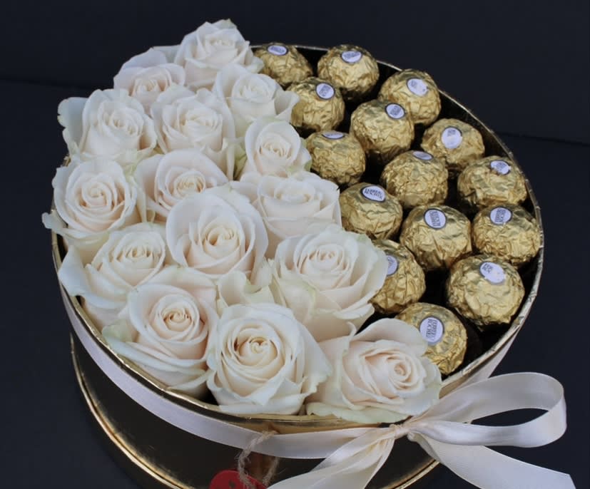 White roses and gold-wrapped chocolates in a round gift box with a ribbon