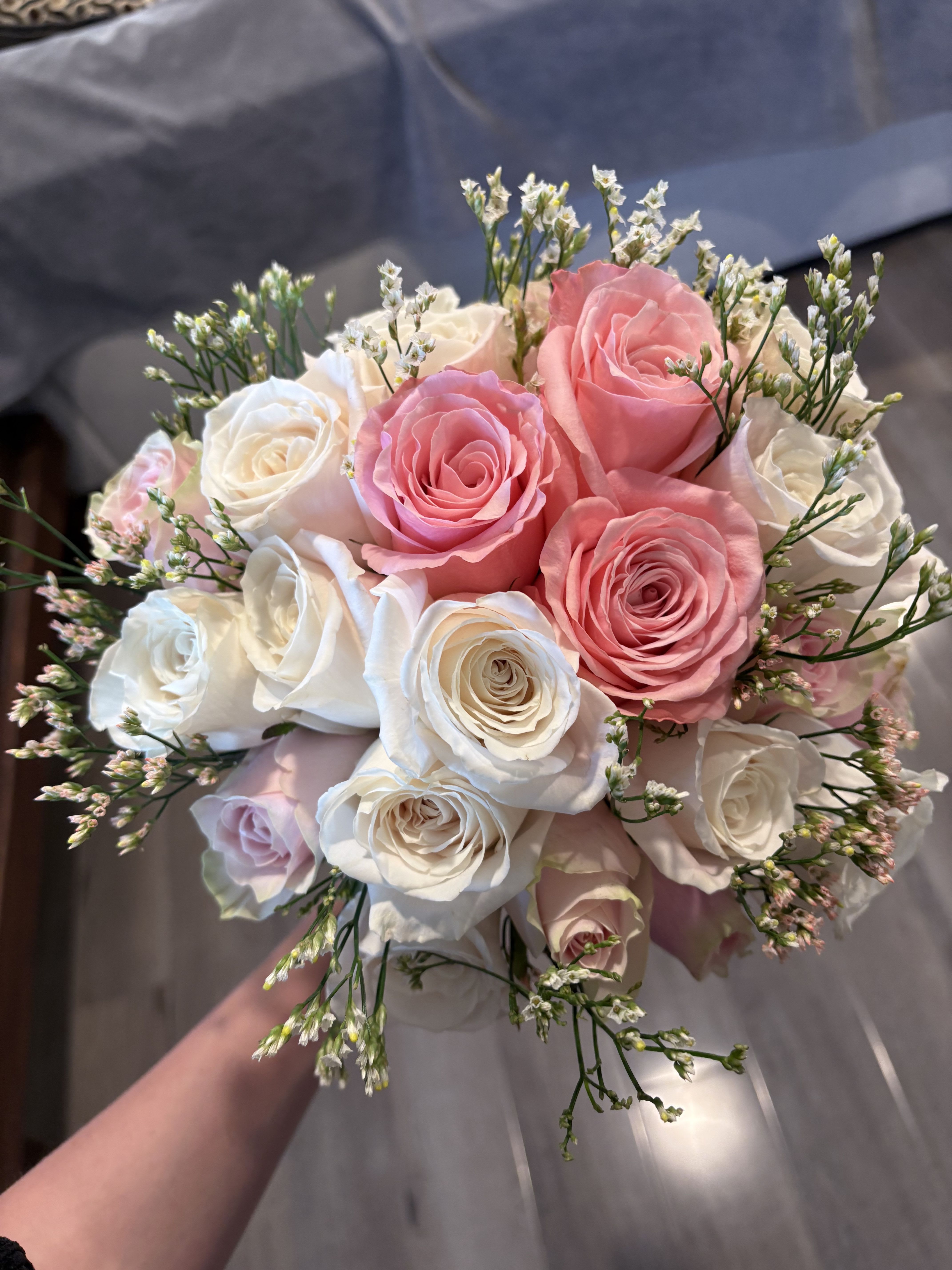 Handheld bouquet of pink and white roses with small filler flowers