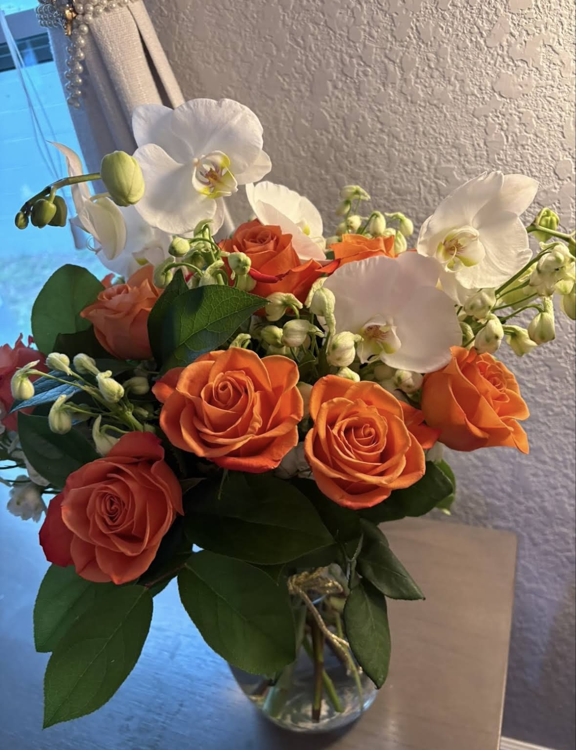 Orange roses and white orchids in a clear glass vase