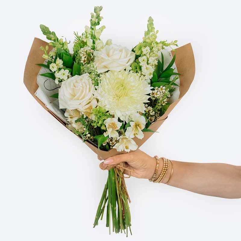 Handheld bouquet of white roses and pale blooms wrapped in brown paper