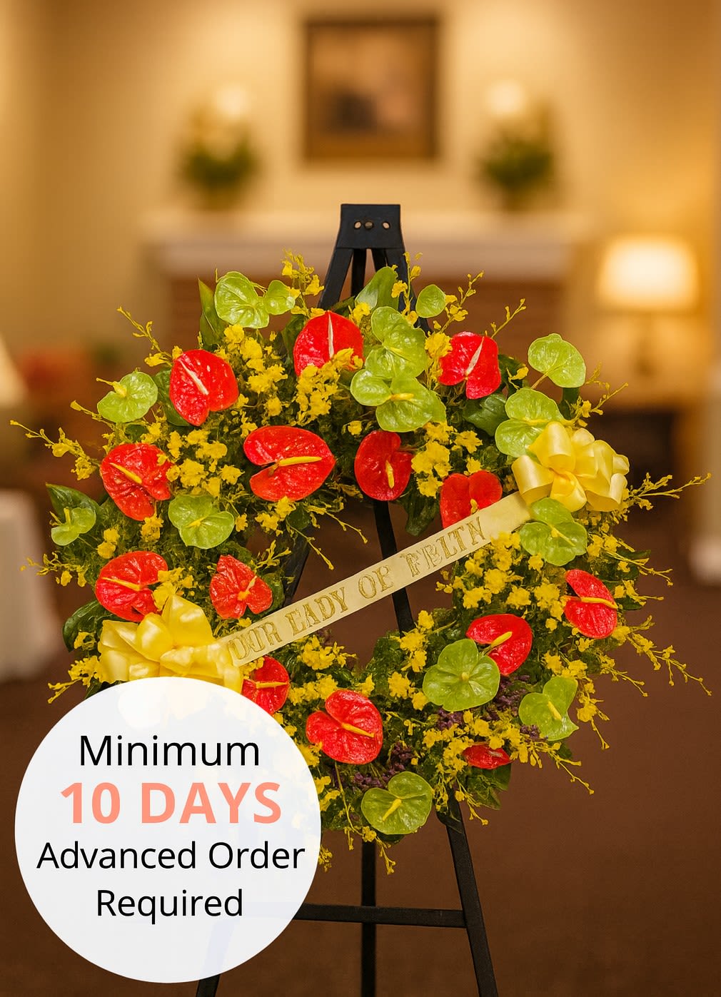 Standing sympathy wreath with red and green tropical blooms and yellow flowers on a black easel.