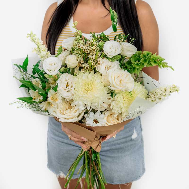 Large bouquet of white flowers with green accents wrapped in brown paper