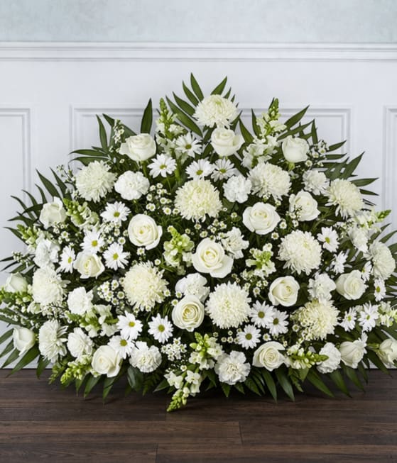 Classic Sympathy Basket - A grand fan-shaped sympathy arrangement in serene all-white blooms-perfect for memorial services and honoring a life with quiet dignity. This sympathy arrangement and funeral spray conveys reverence and comfort; the person you're remembering will be honored by its formal silhouette and calm, monochromatic presence.  Open white roses, round chrysanthemums, carnations, daisies, and snapdragons are densely clustered for a richly textured, full look. The low-to-medium height presentation is framed by an arc of dark, elongated greenery that gives structure and a gentle, upright form fitting for a casket spray or standing tribute. The varied flower shapes-pillowy roses, ruffled carnations, spidery mums, delicate daisies, and vertical snapdragons-create depth while keeping the overall tone peaceful and unified.  Send this arrangement to express sympathy, offer condolences at a funeral, or as a comforting memorial gift for grieving family members. It arrives ready to display; minimal care is needed beyond keeping flowers cool and out of direct sun for as long as possible to preserve their clean, tranquil presence.
