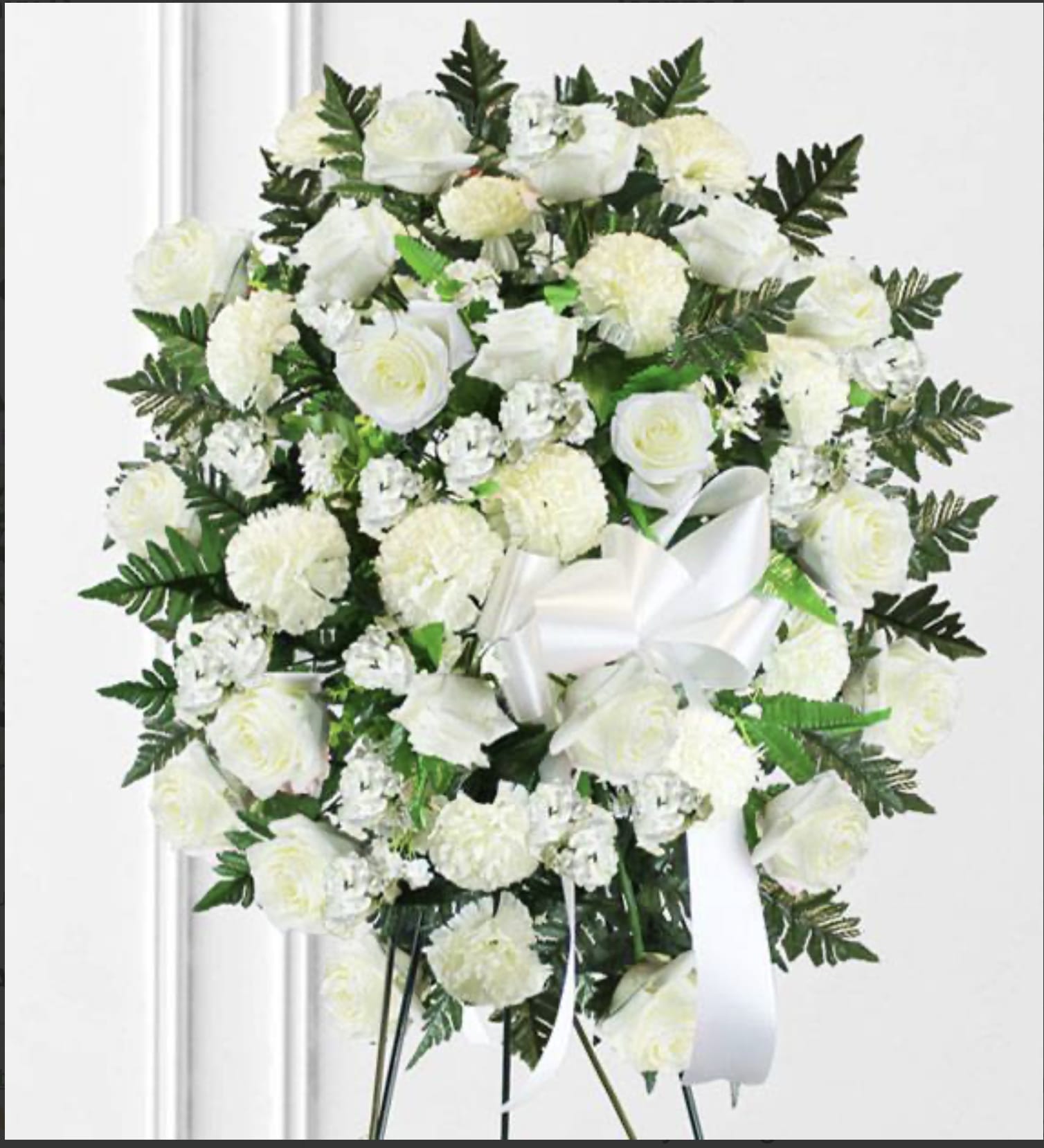 White rose and carnation standing spray with a white ribbon