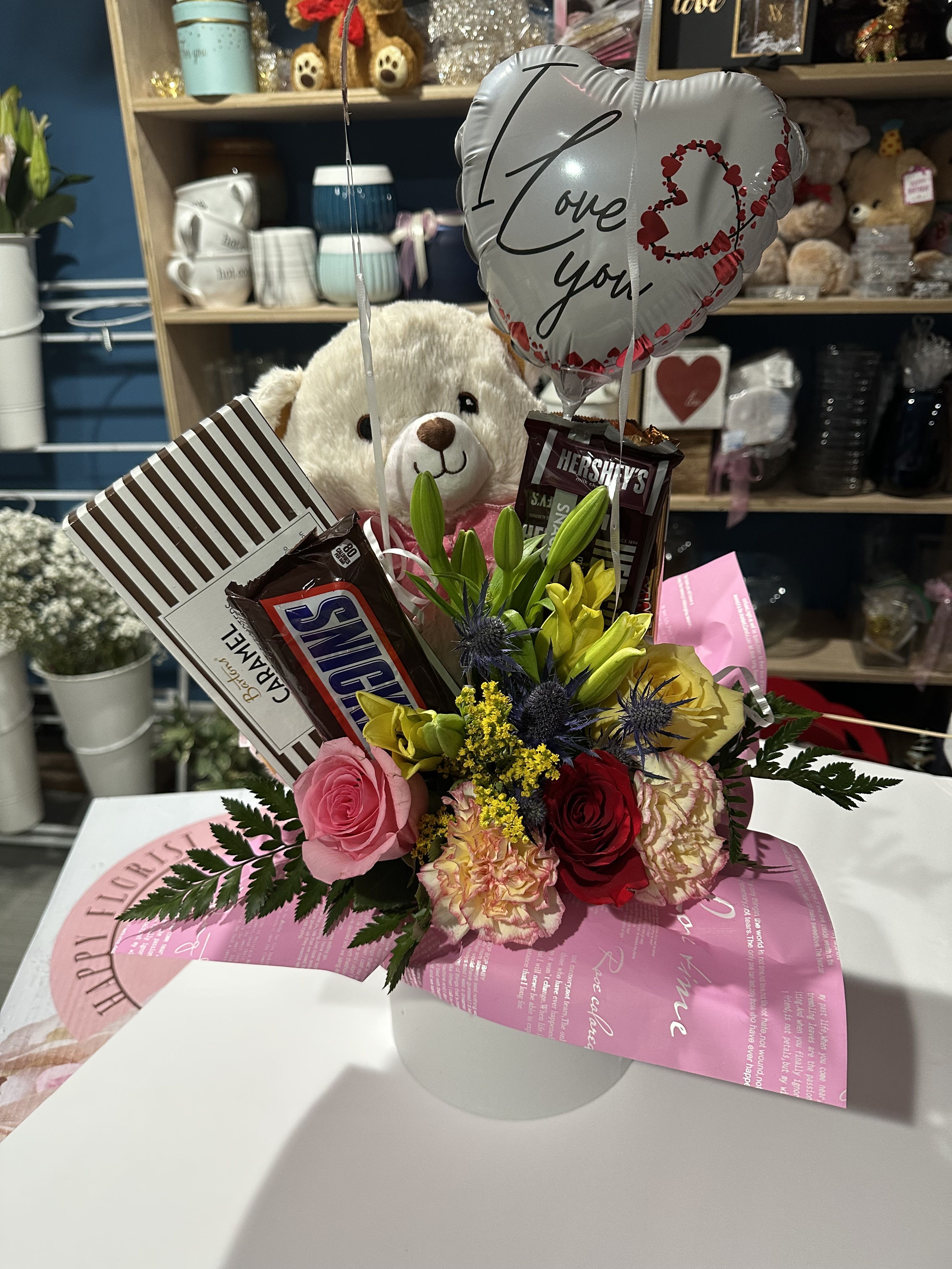 Flower and candy gift arrangement with a teddy bear and heart balloon