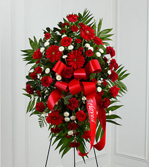 The FTD Treasured Memories Standing Spray - The FTD® Treasured Memories™ Standing Spray is a rich and colorful way to express your unending love and devotion to the departed. An exceptional arrangement of red roses, burgundy carnations, burgundy mini carnations, red gerbera daisies and white button poms are accented with a variety of lush greens. A red ribbon with the word, "Beloved", embossed in a gold metallic lettering, finishes this beautiful display for their final farewell service. Displayed on a wire easel. Approximately 46"H x 30"W. Your purchase includes a complimentary personalized gift message.