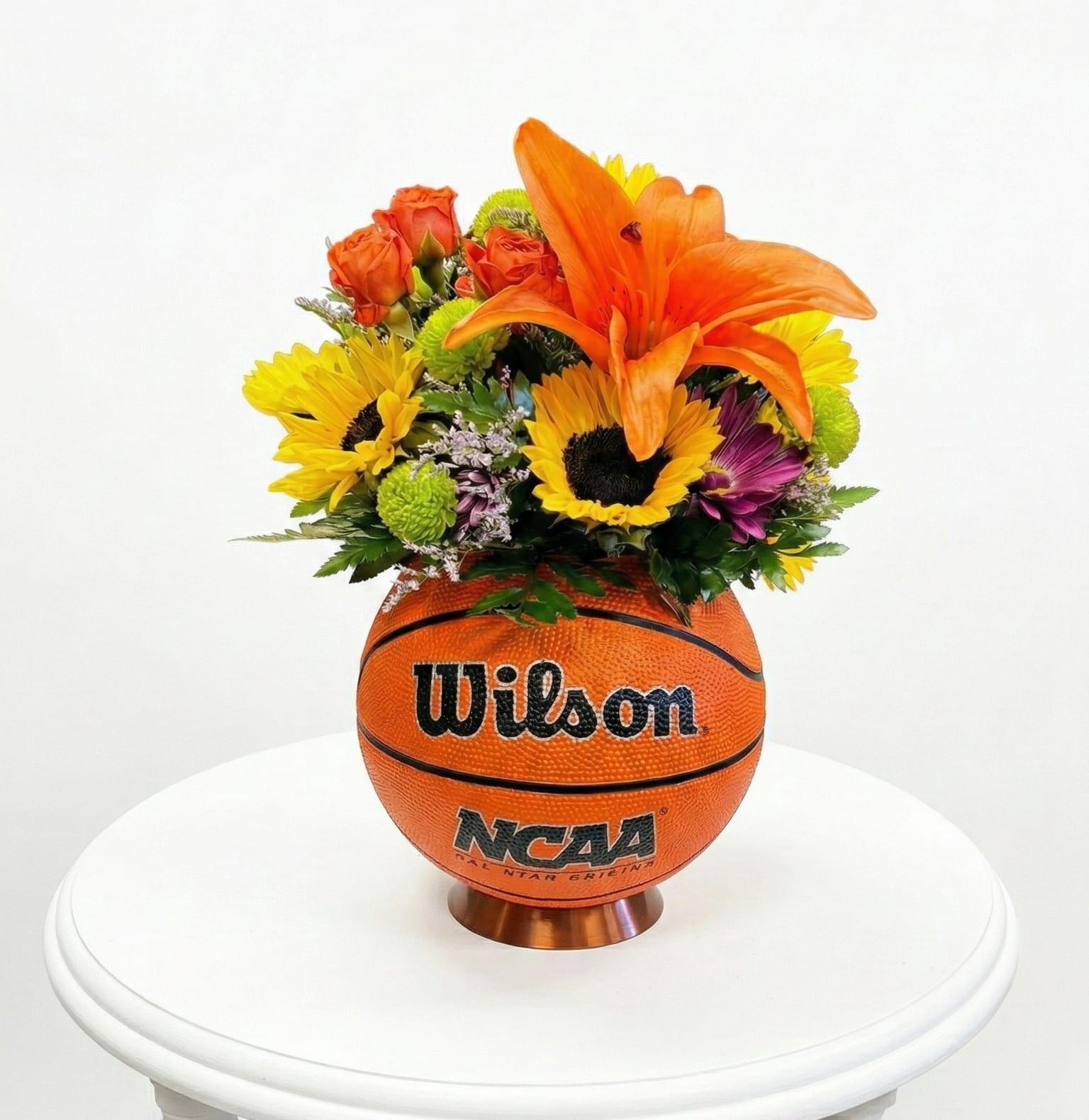 Flower arrangement in a basketball-shaped container with orange lilies and sunflowers