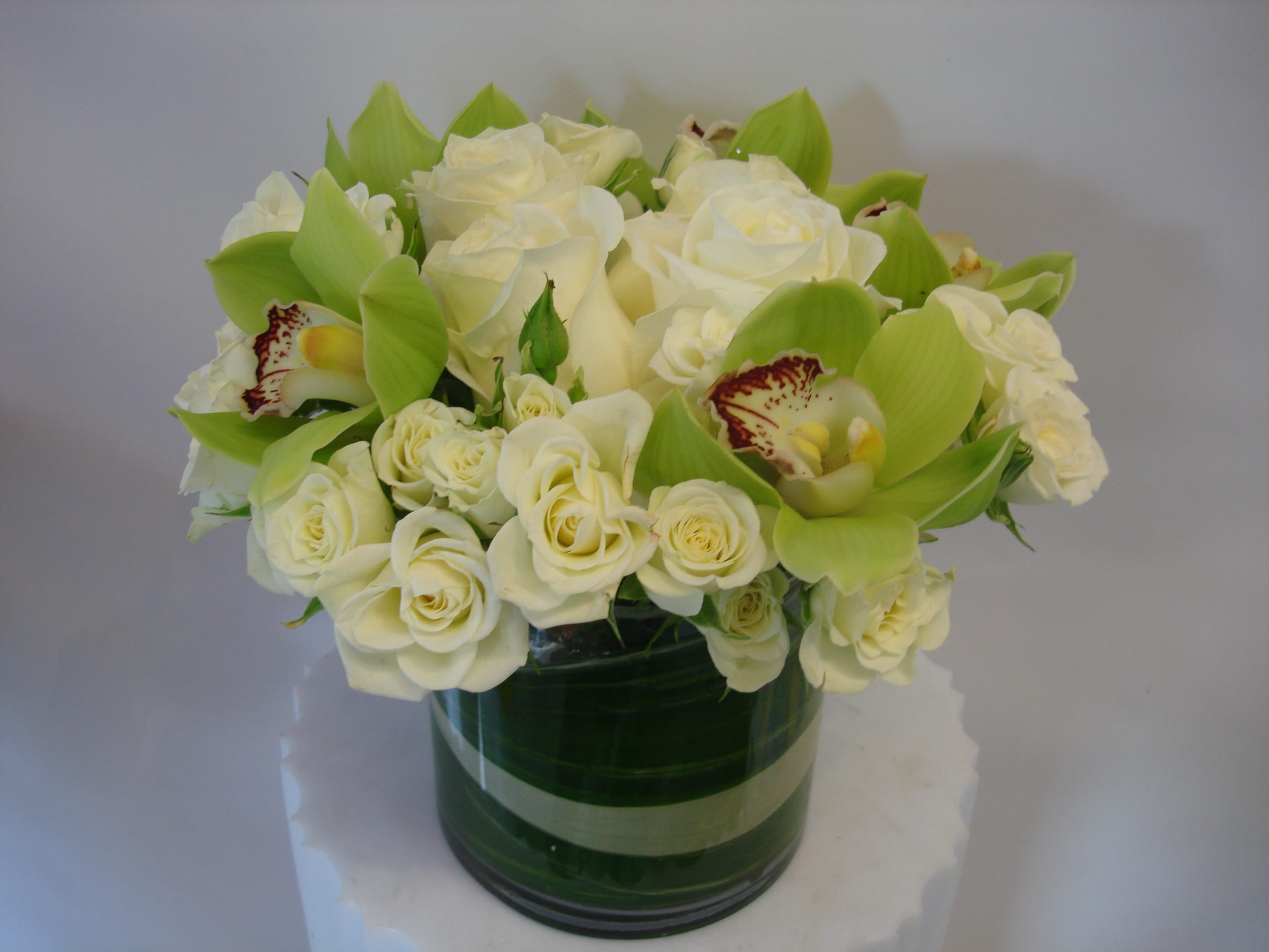 White roses and green orchids arranged in a glass vase