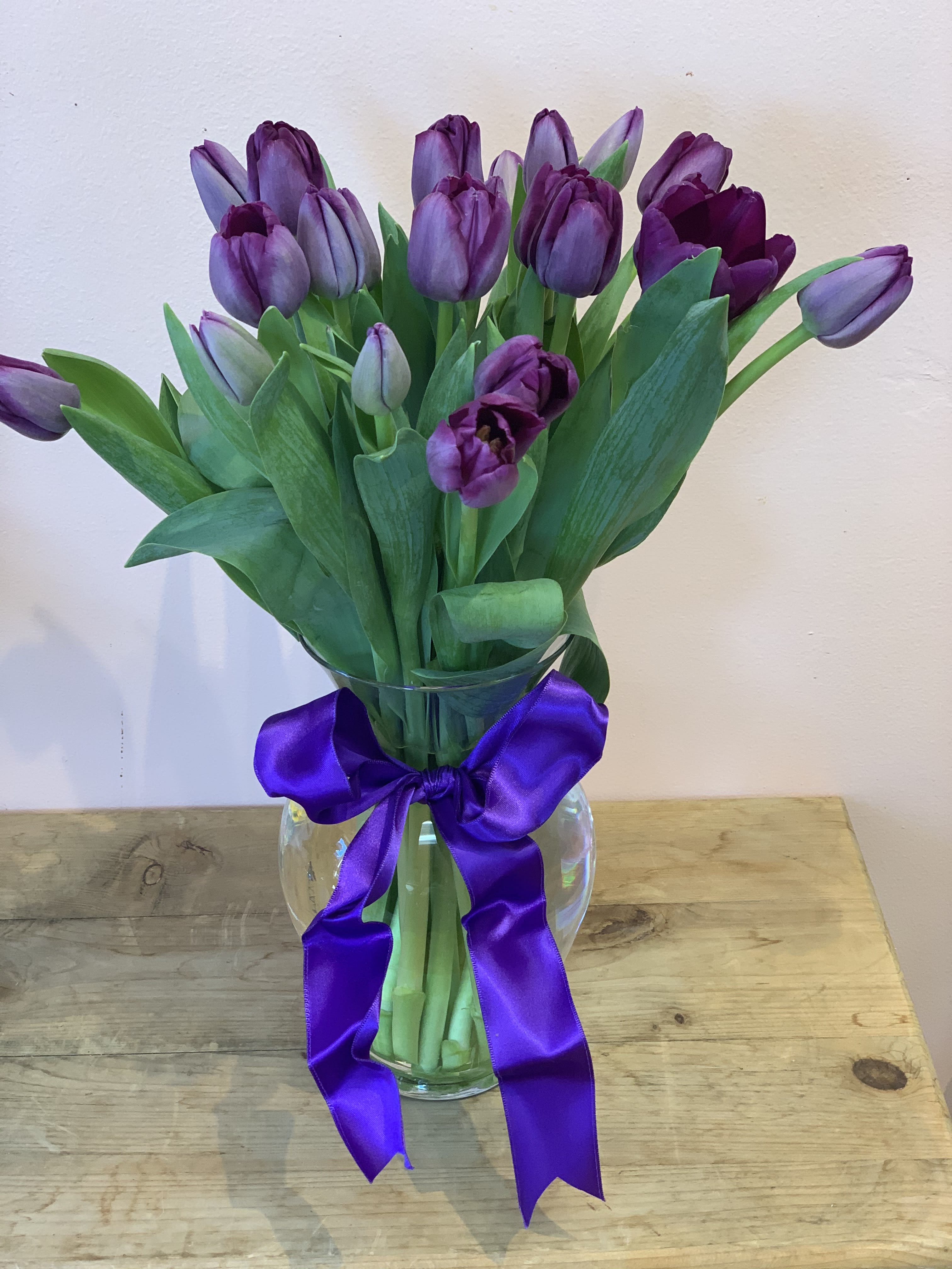 Purple tulips in a clear glass vase with a purple ribbon bow