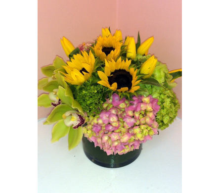 Bouquet of sunflowers, yellow lilies, and pink hydrangeas in a dark vase