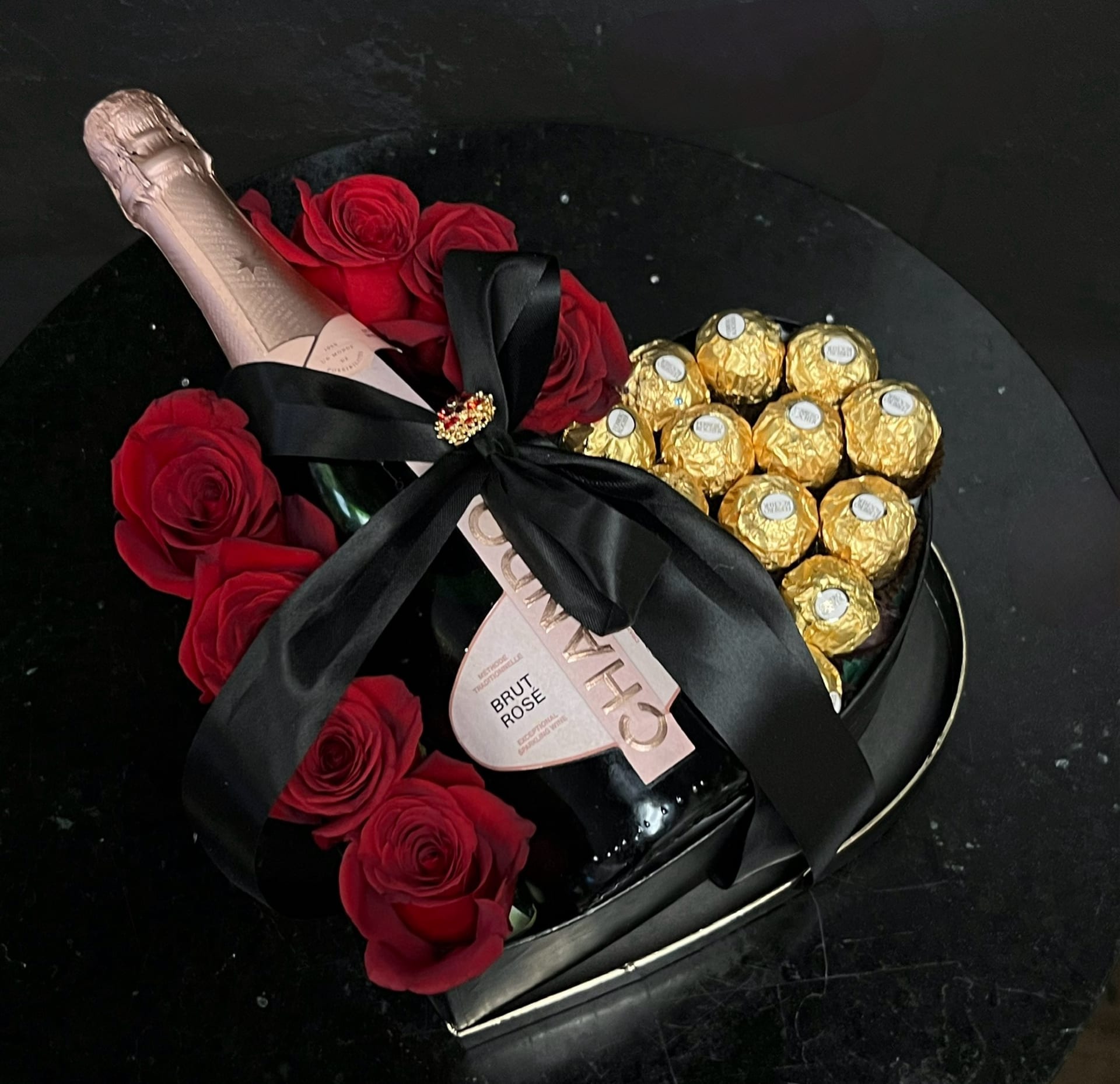 Heart-shaped gift box with red roses, champagne, and gold-wrapped chocolates