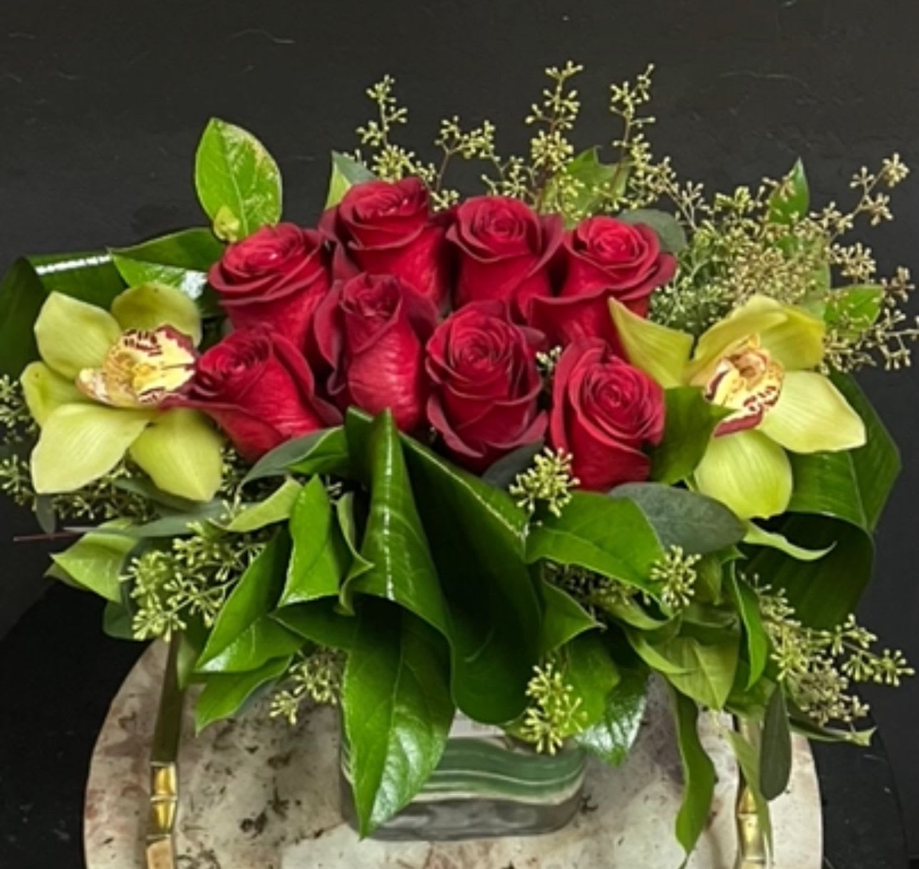 Red roses with pale green orchids in a low vase arrangement